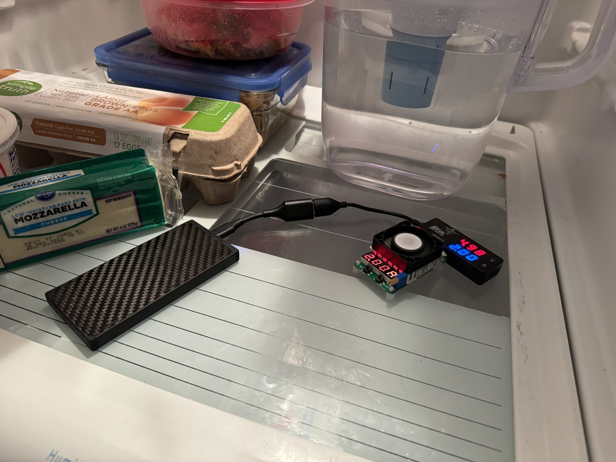 The Nitecore power bank is hooked up to a multimeter and dummy resistor load inside a refrigerator with food.