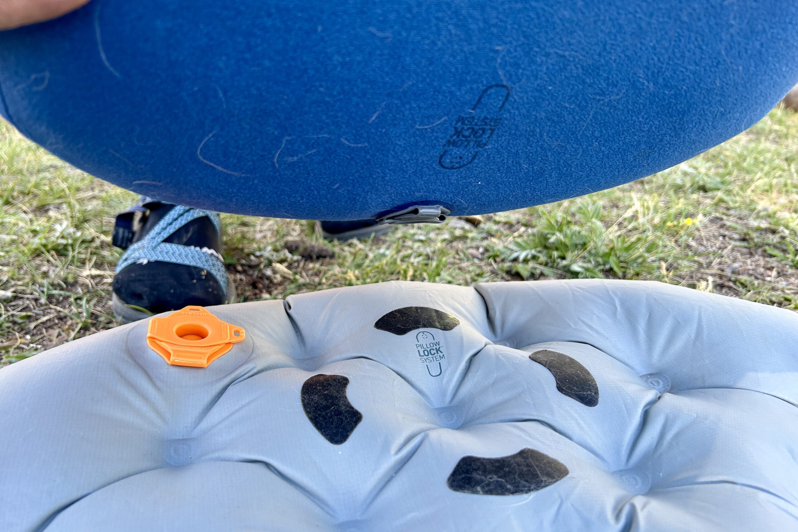 A person holds a small inflatable pillow above a sleeping pad.