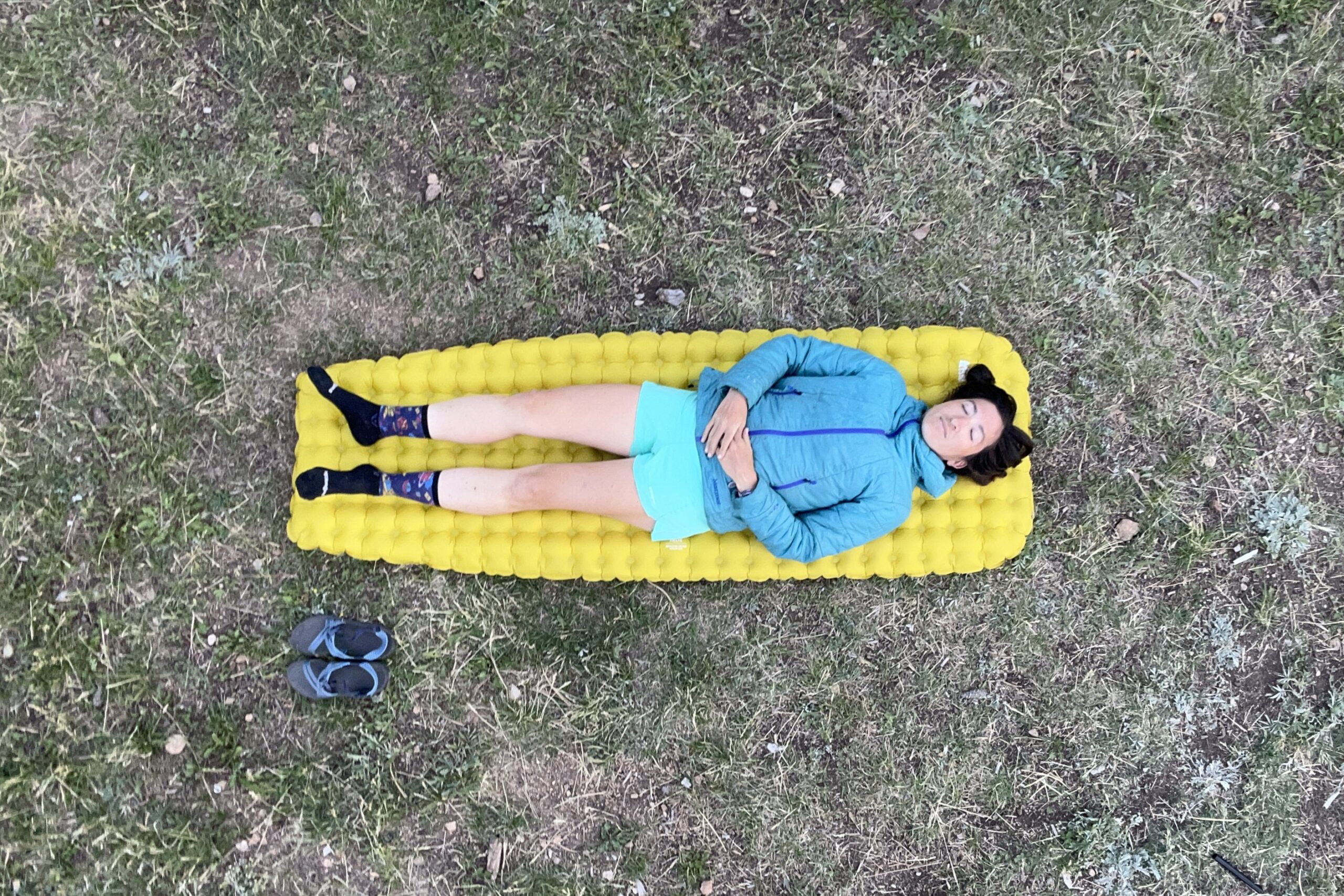 A woman is lying on an inflatable mattress on the grass on a sunny day.