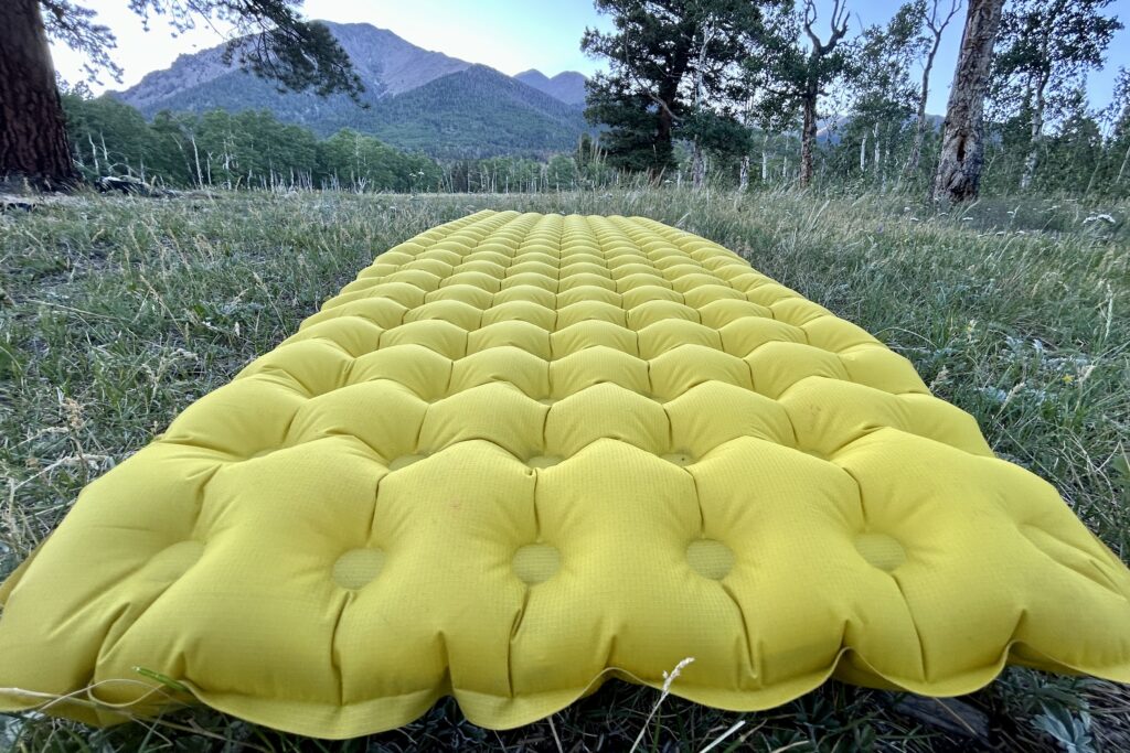 Close up of a yellow inflatable camping pad in the grass with mountains in the background.