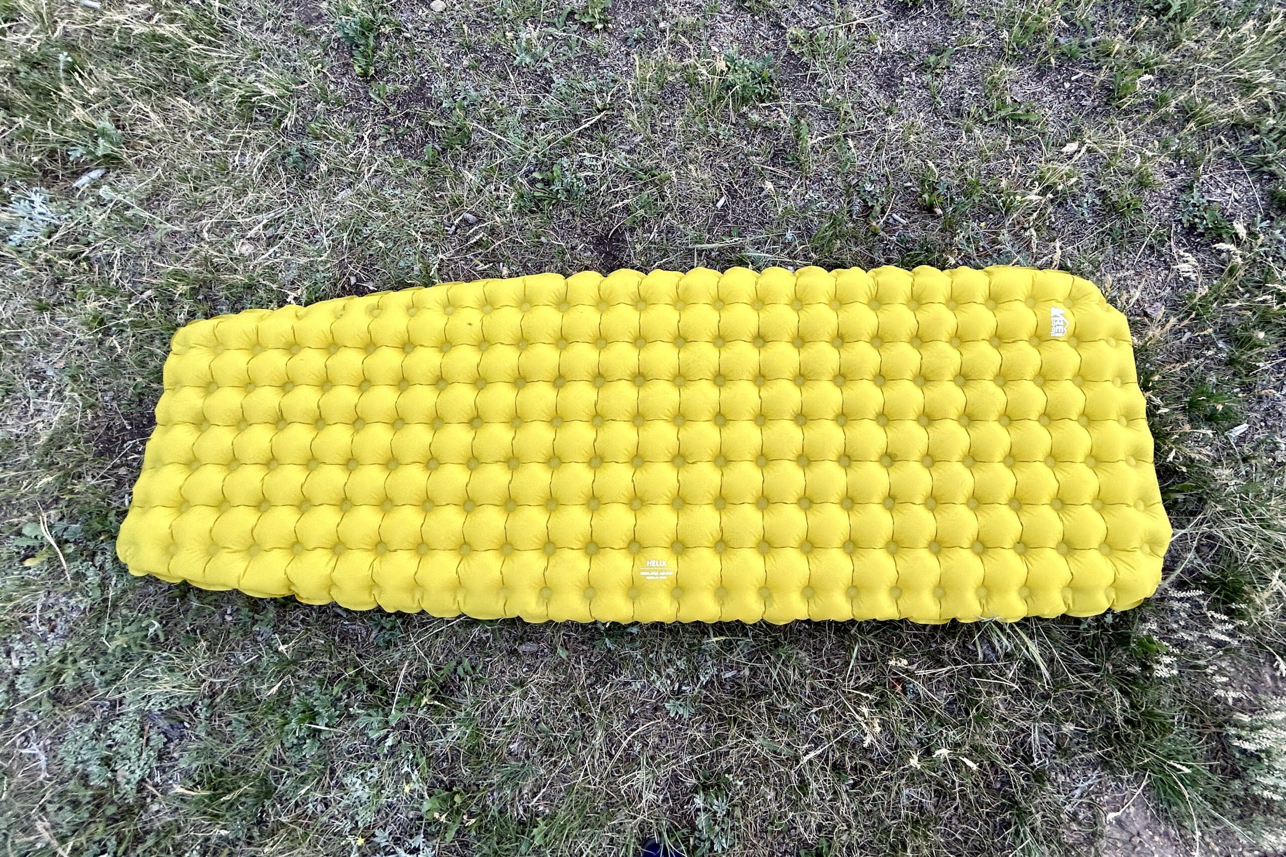 A yellow sleeping pad lies flat on the ground.