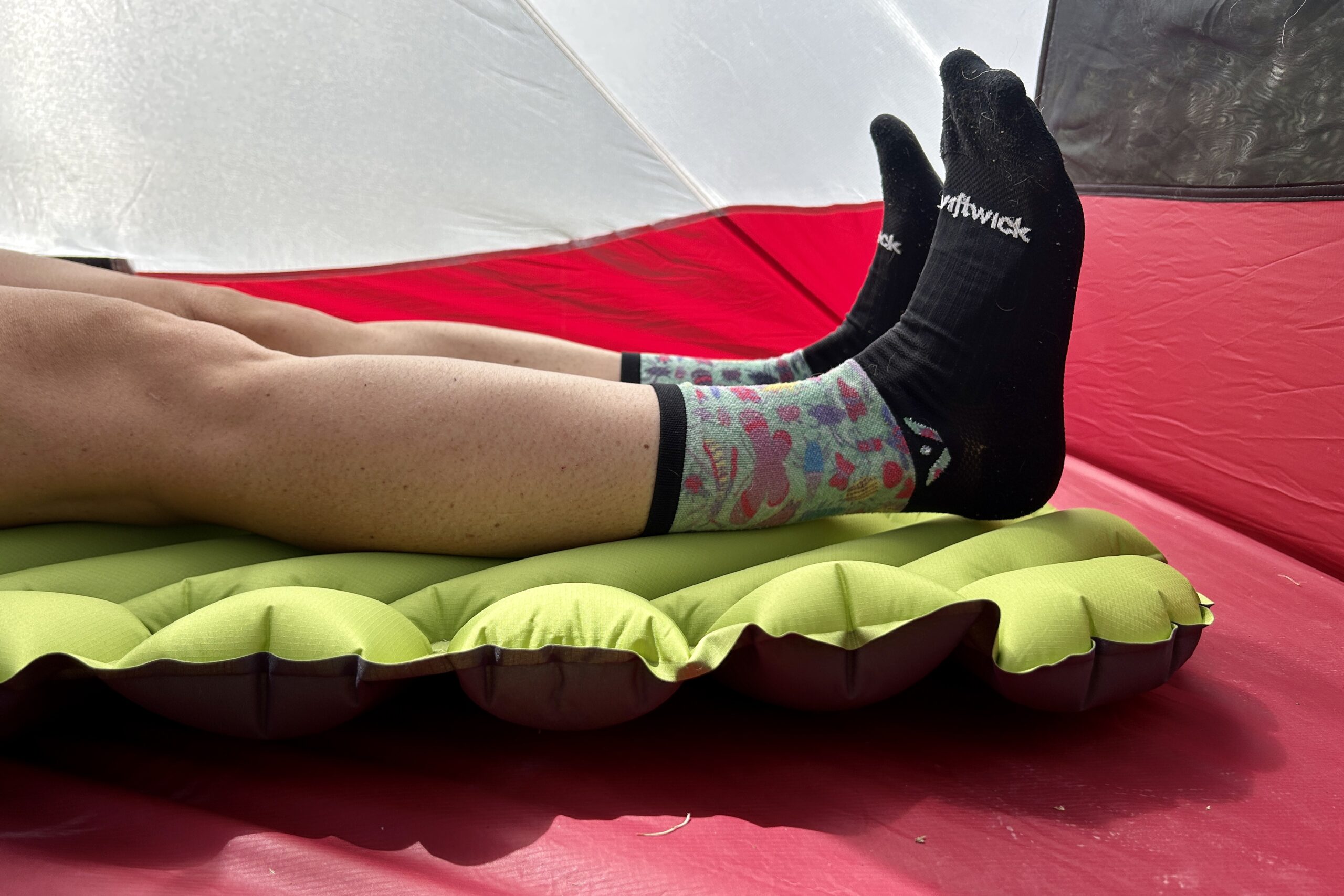 Close up of a person's feet reclining comfortably on a vibrant green air pad in a red and white tent.