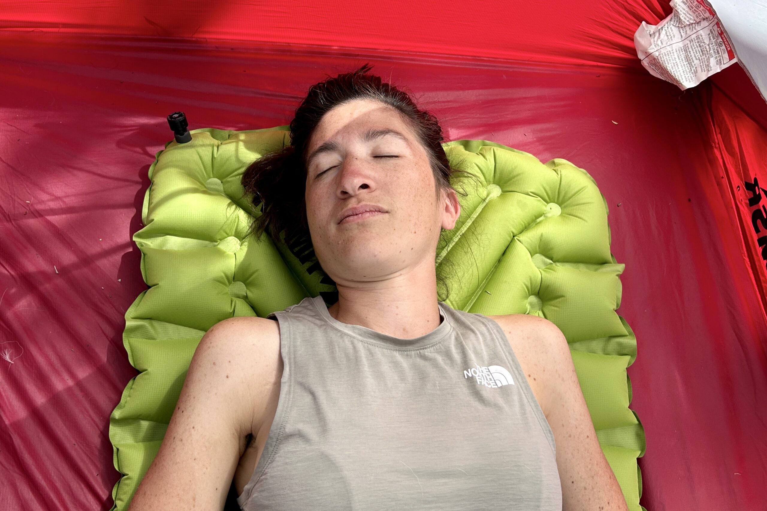 A woman rests comfortably on an air pad in a tent.