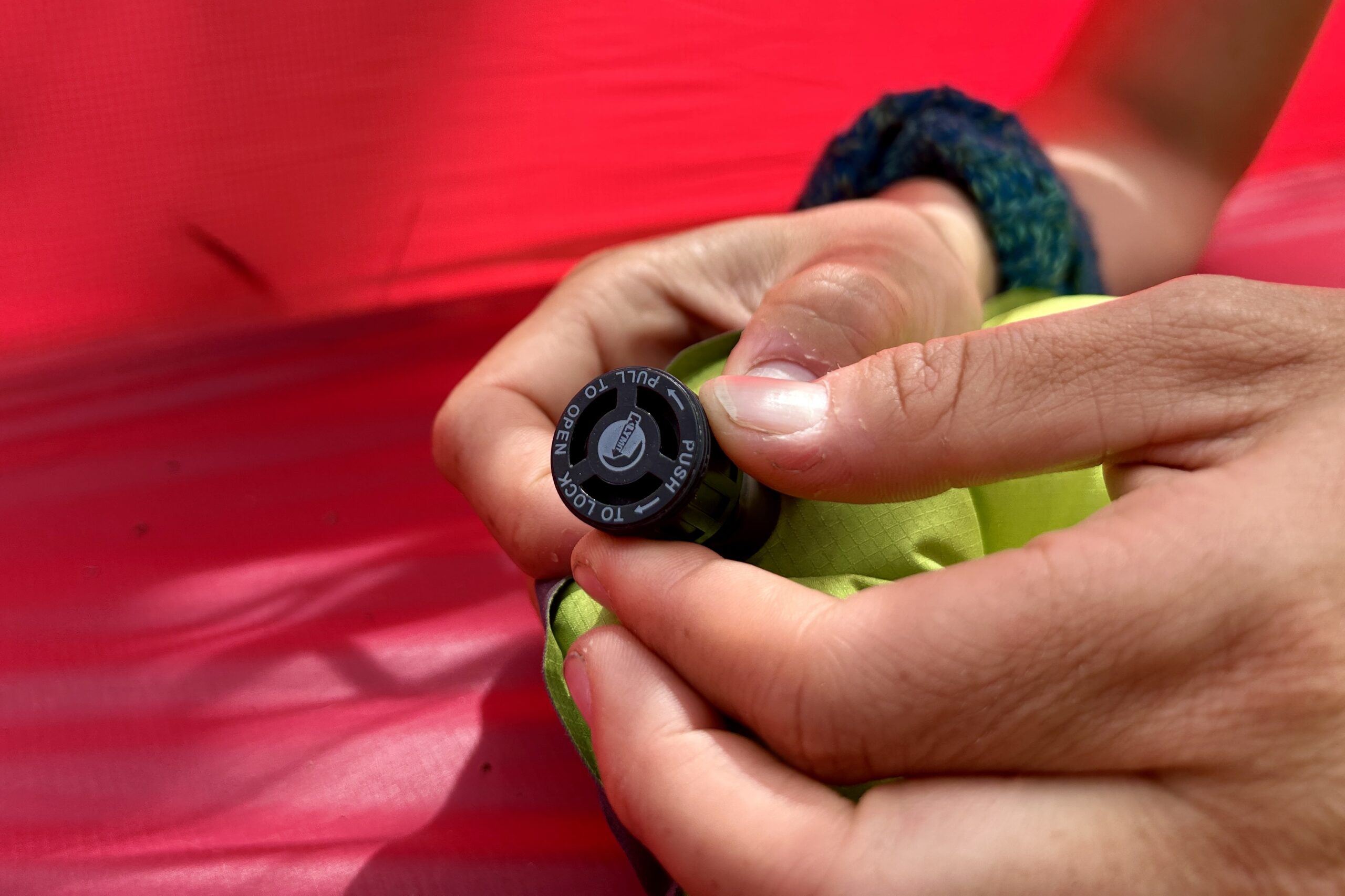 A person holds a small black valve for a sleeping pad in their hands.