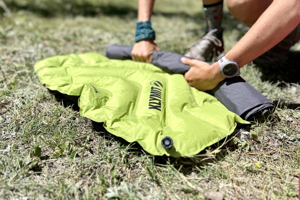 A person rolls up a sleeping pad on the ground.