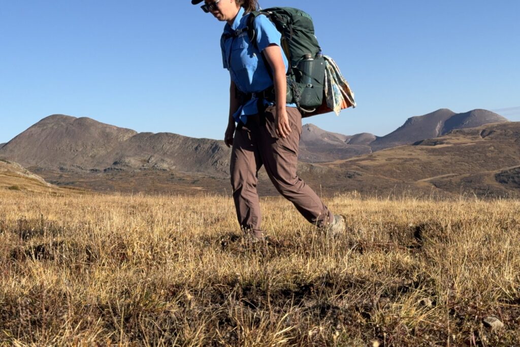 A hiker wearing the Mountain Hardwear Dynama 2 pants walks on a trail in the mountains.