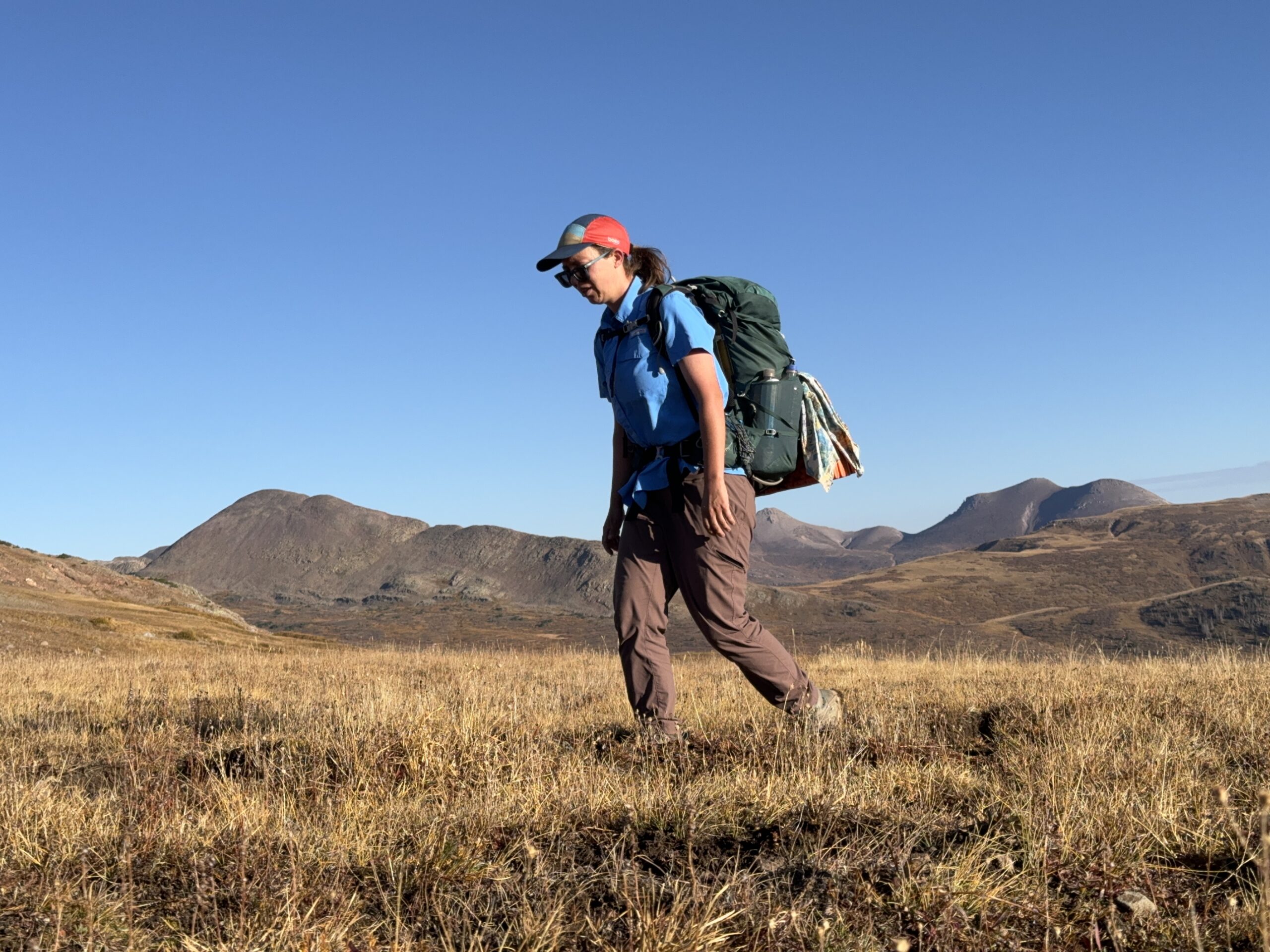 A hiker wearing the Mountain Hardwear Dynama 2 pants walks on a trail in the mountains.