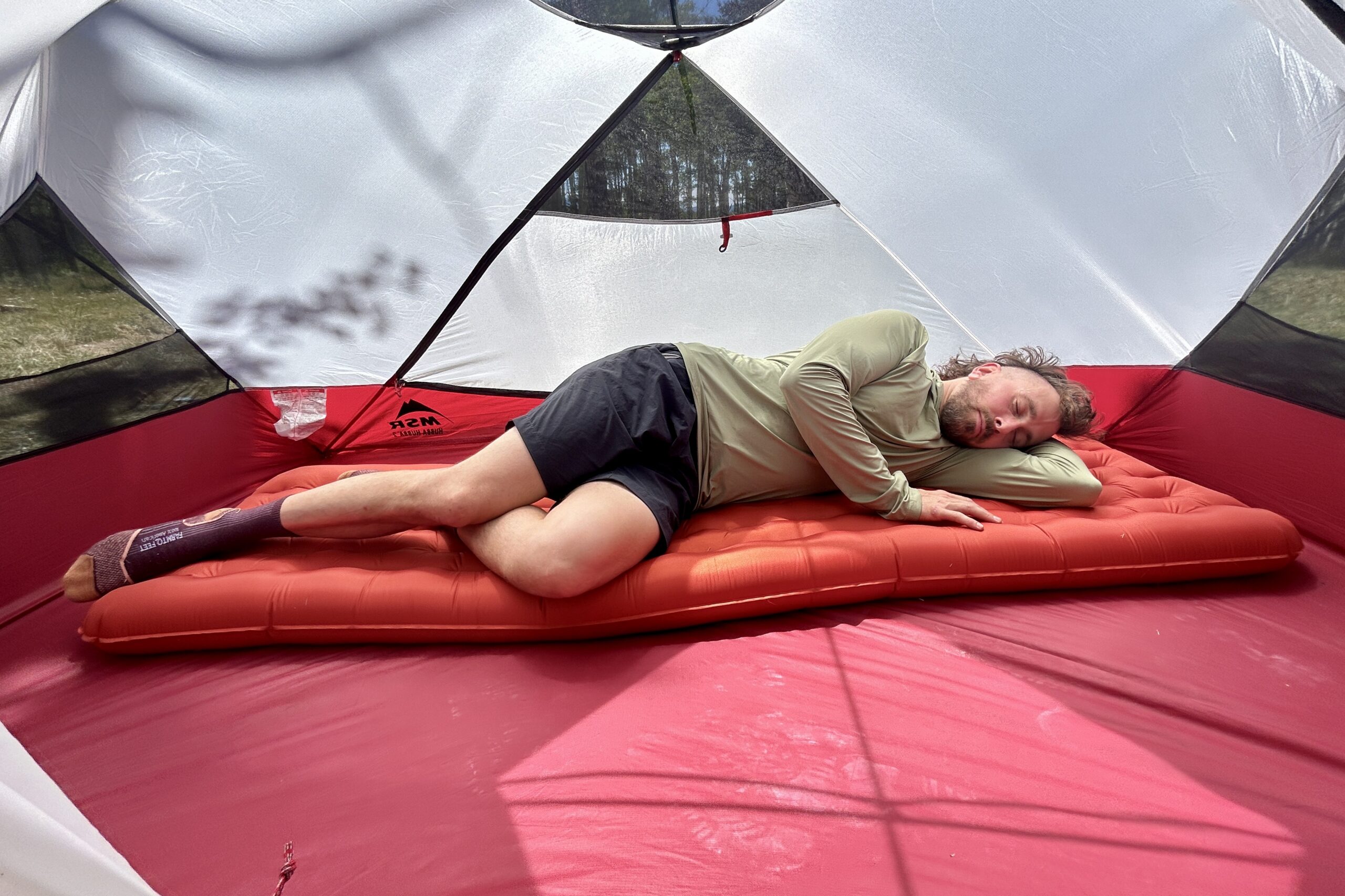 A person sleeps on their side on a red inflatable sleeping pad inside a tent.