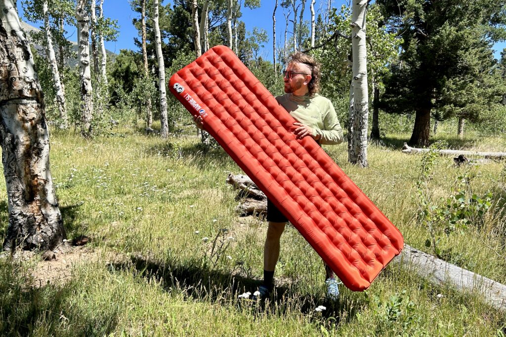 A man stands in the woods holding a red inflatable air pad.