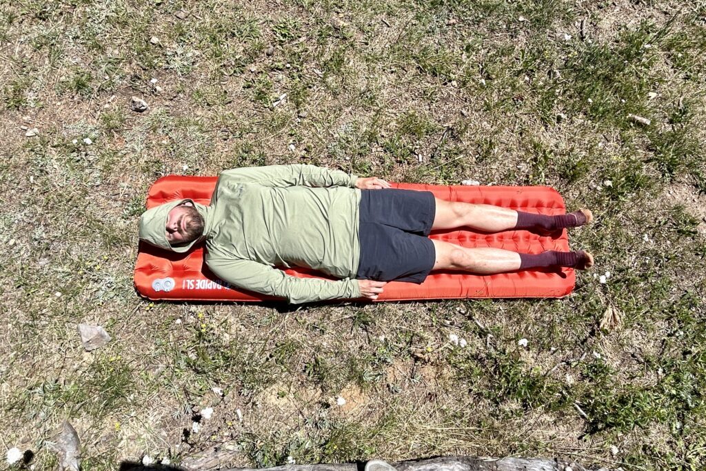 A man is lying on an inflatable mattress on the grass on a sunny day.