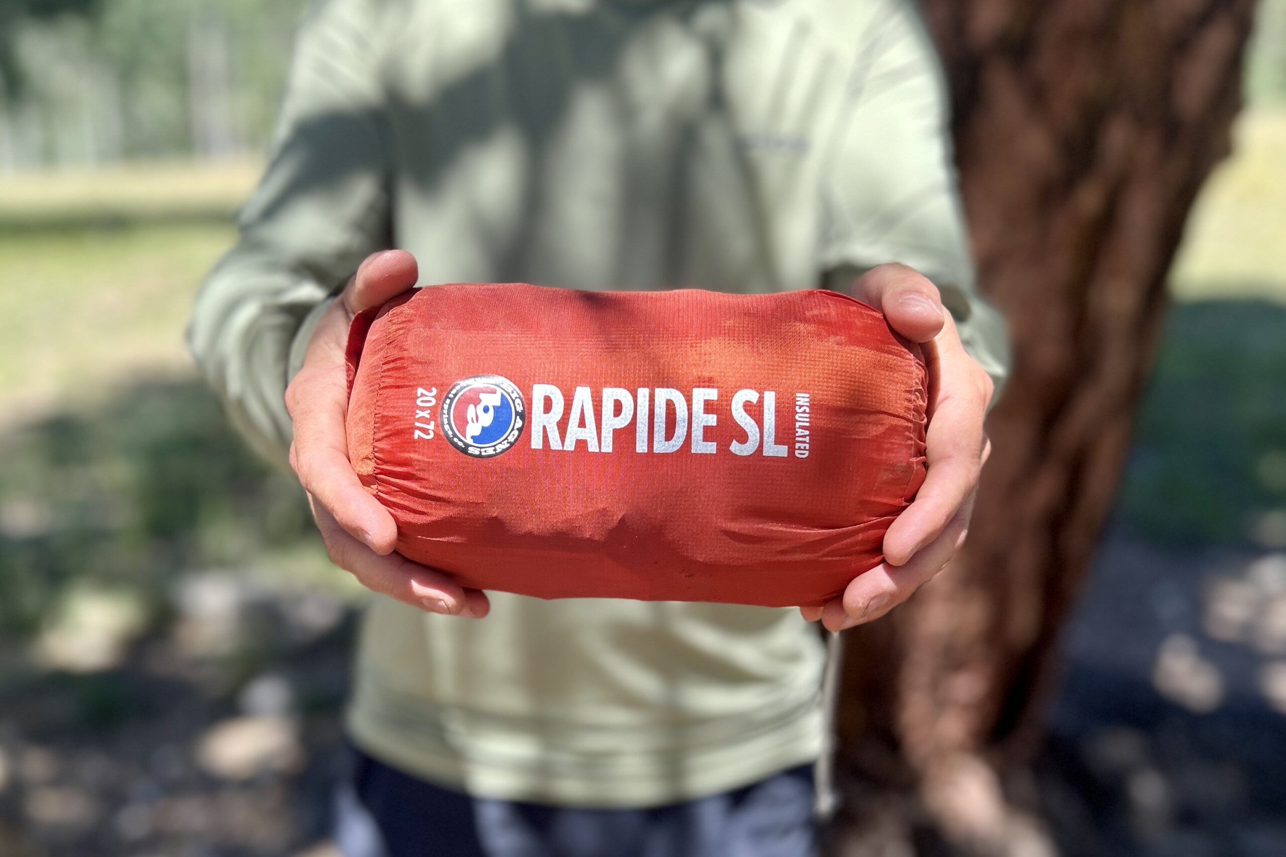 A man holds a small red stuff sack labeled "Rapide SL".