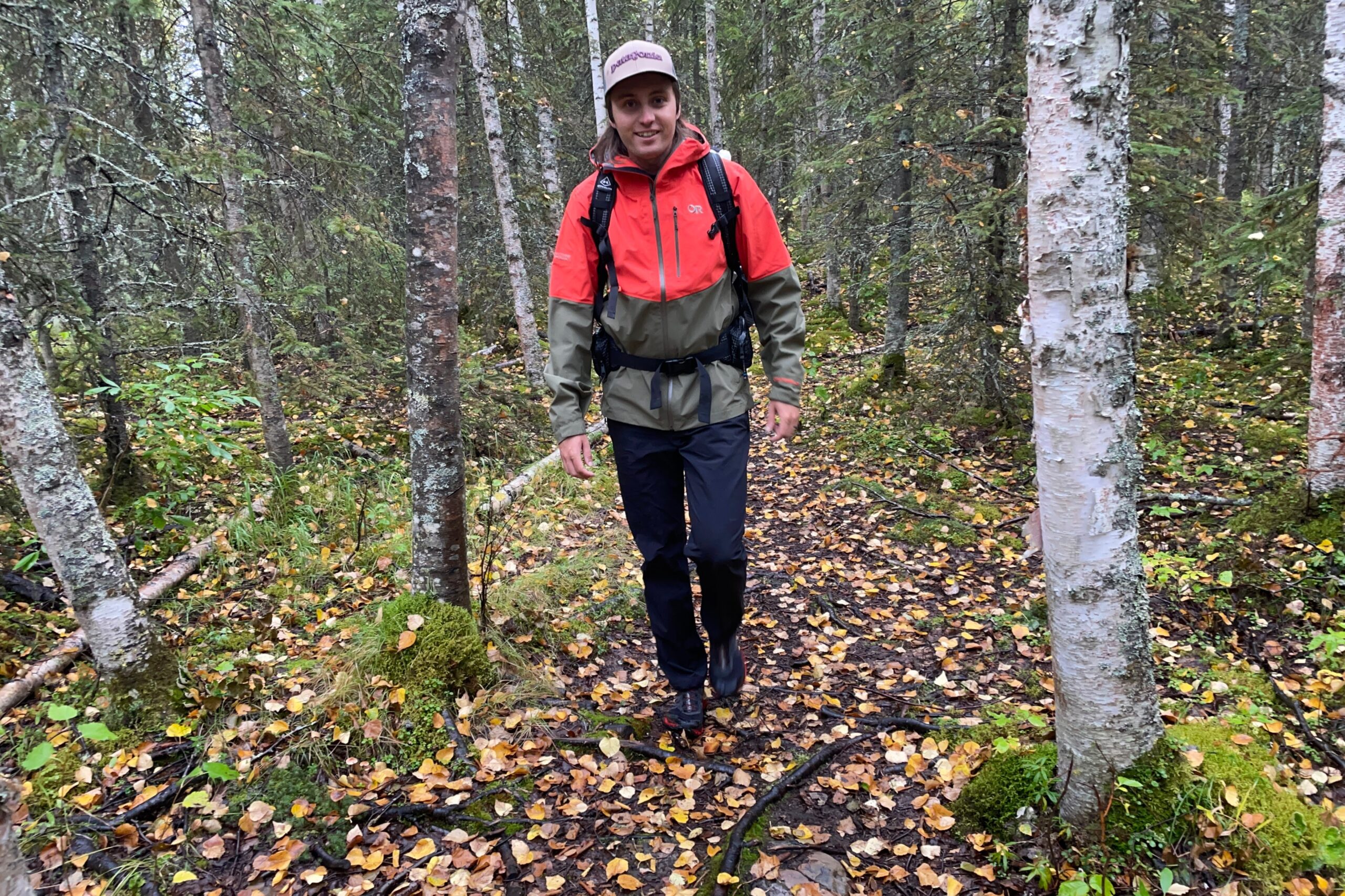 A man walks through a forest with yellow leaves on the ground.