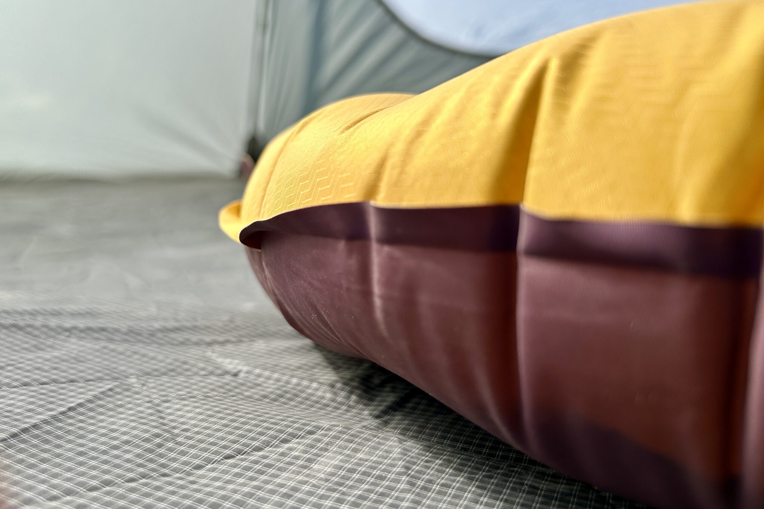 Very close up image of a the side and thickness of a yellow and brown sleeping pad in a tent