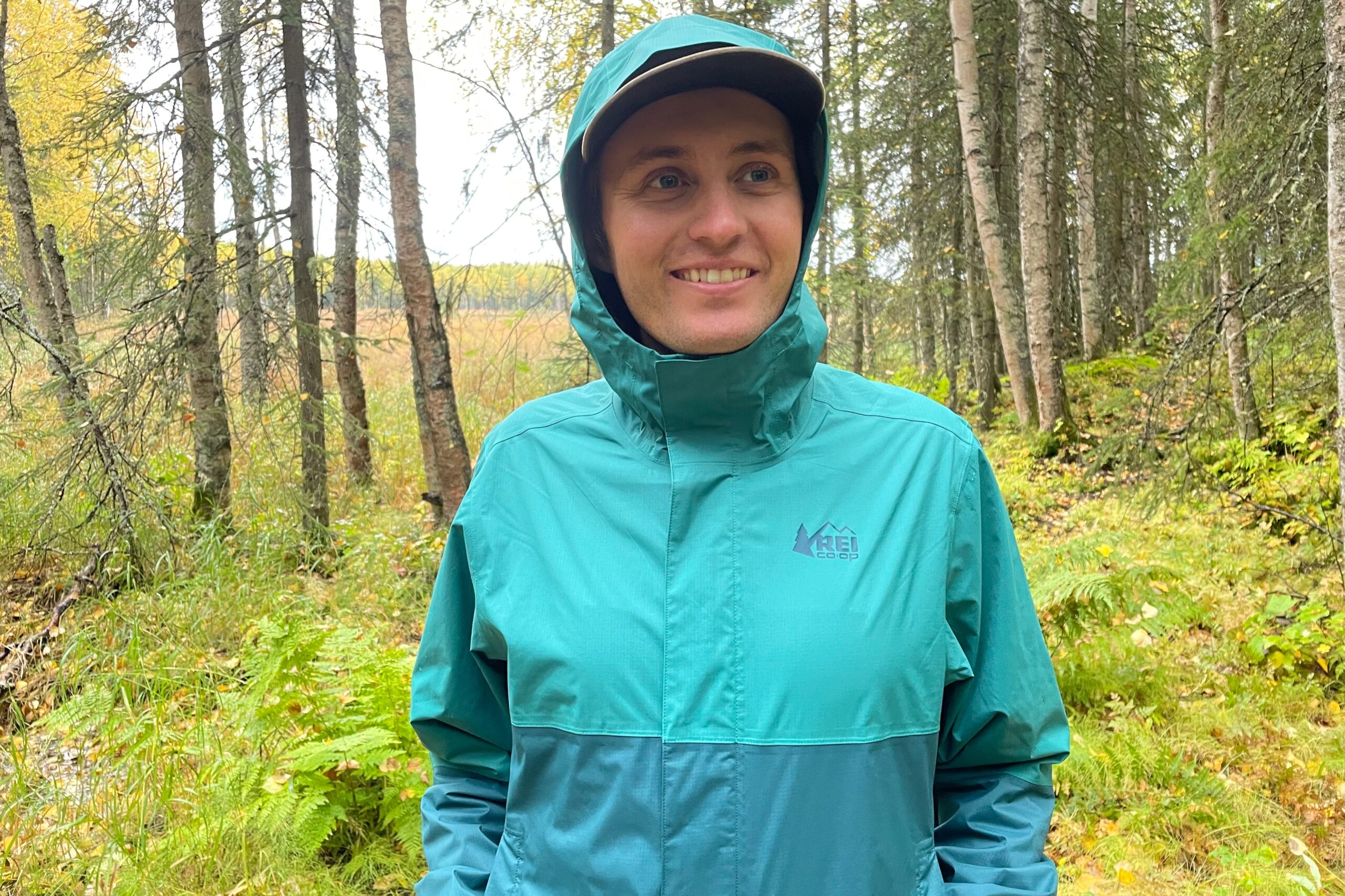 A man wearing a rain jacket smiles in front of a meadow.