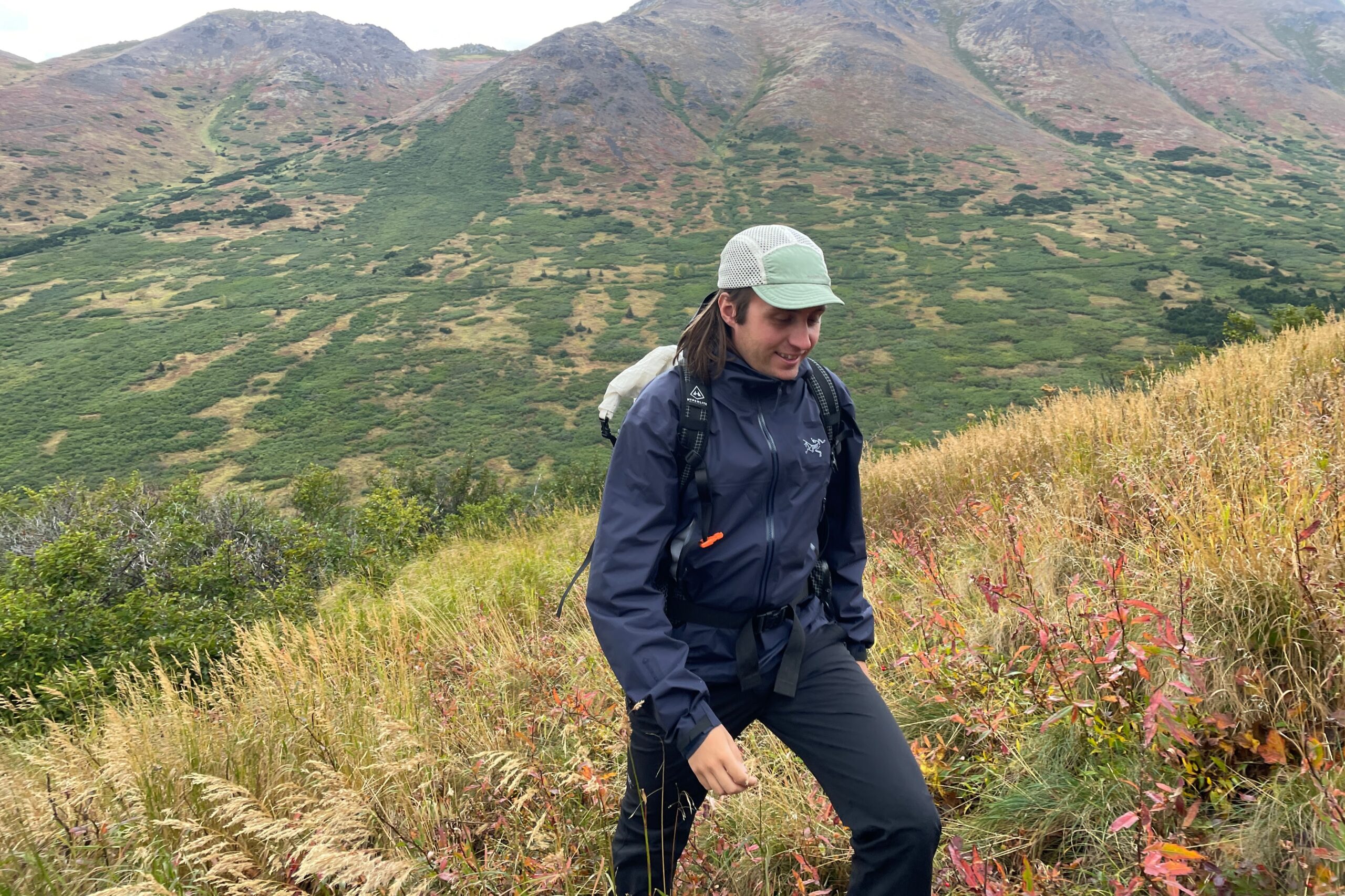 A man walks offt rail through tall grass wearing rain gear.