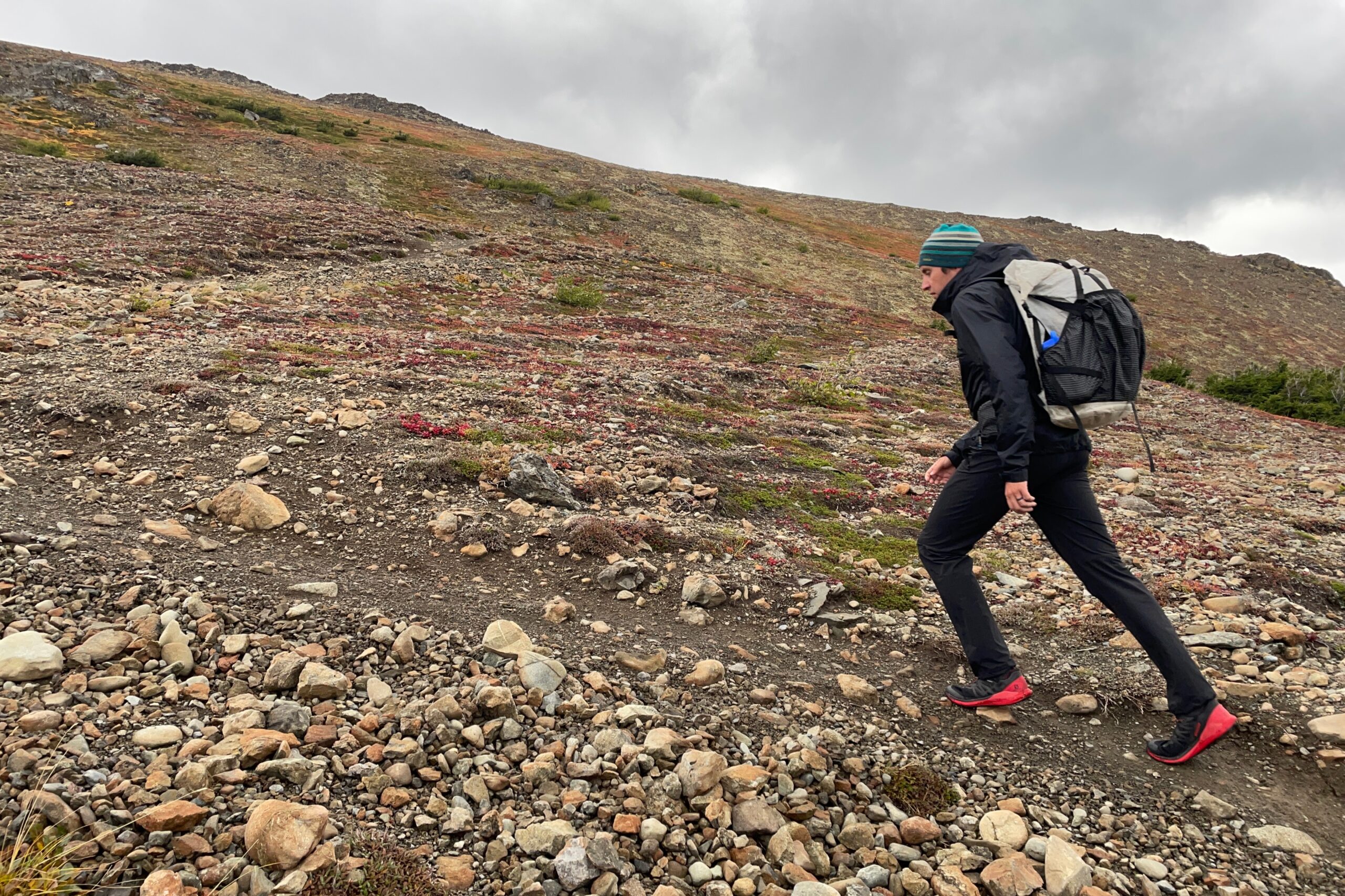 A man hikes uphill on an alpine trail under cloudy skies