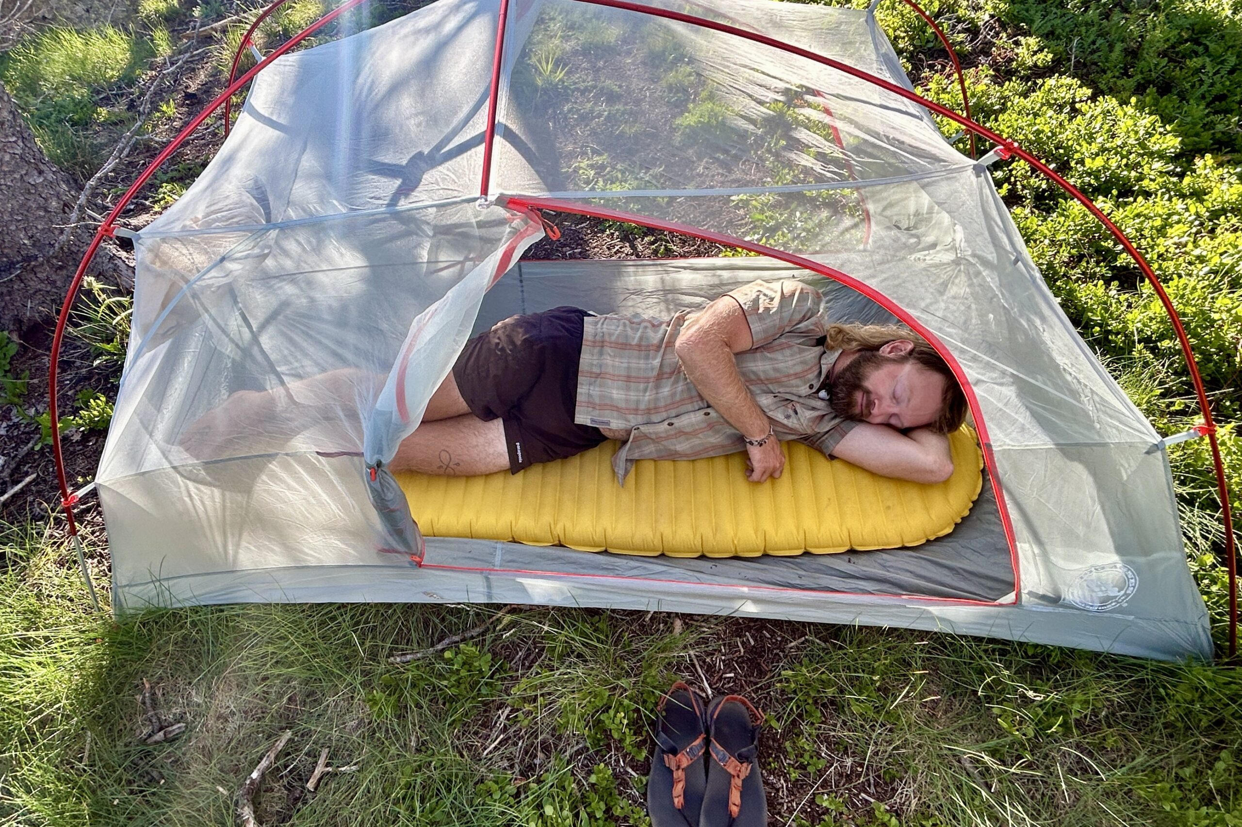 A person lies asleep in a tent on their side on a bright yellow sleeping pad.