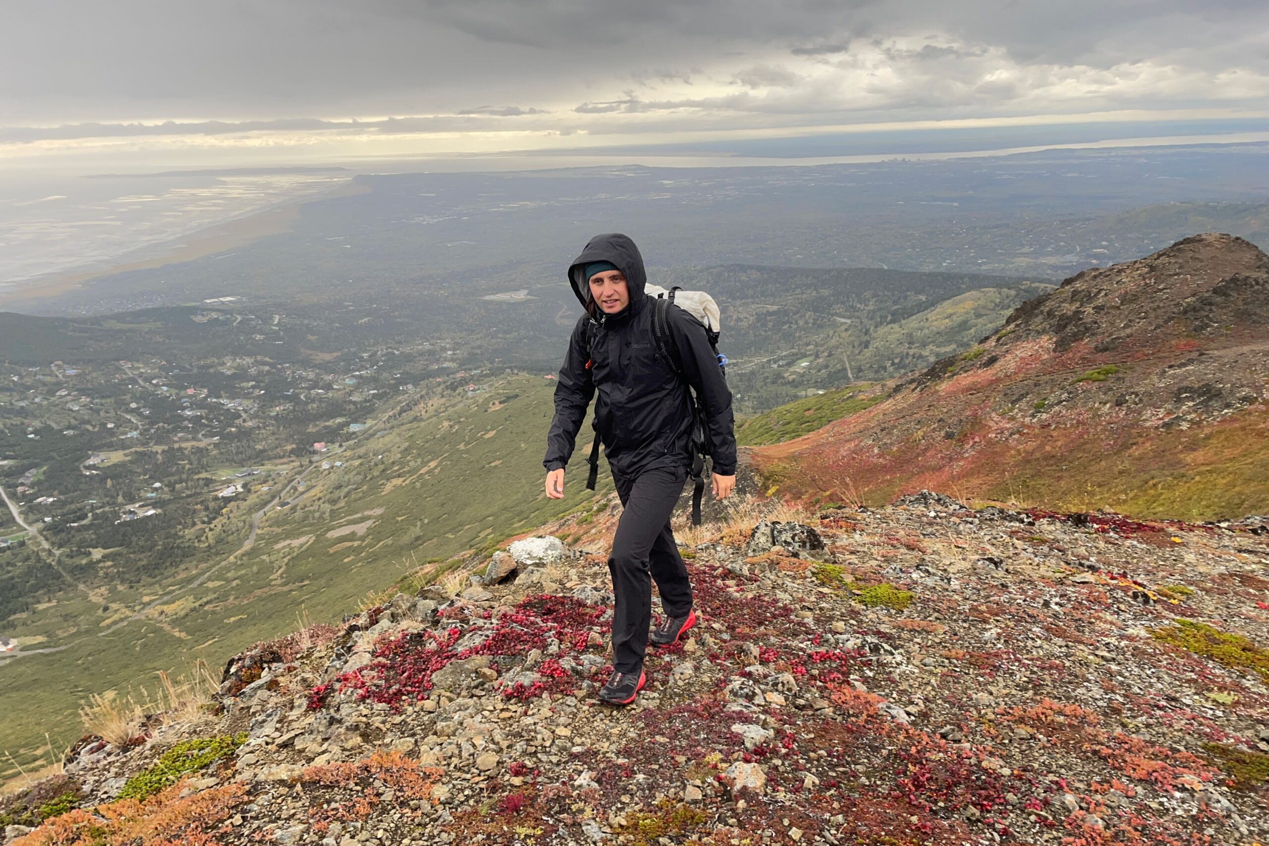 A man hikes uphill with a coastal view behind him.