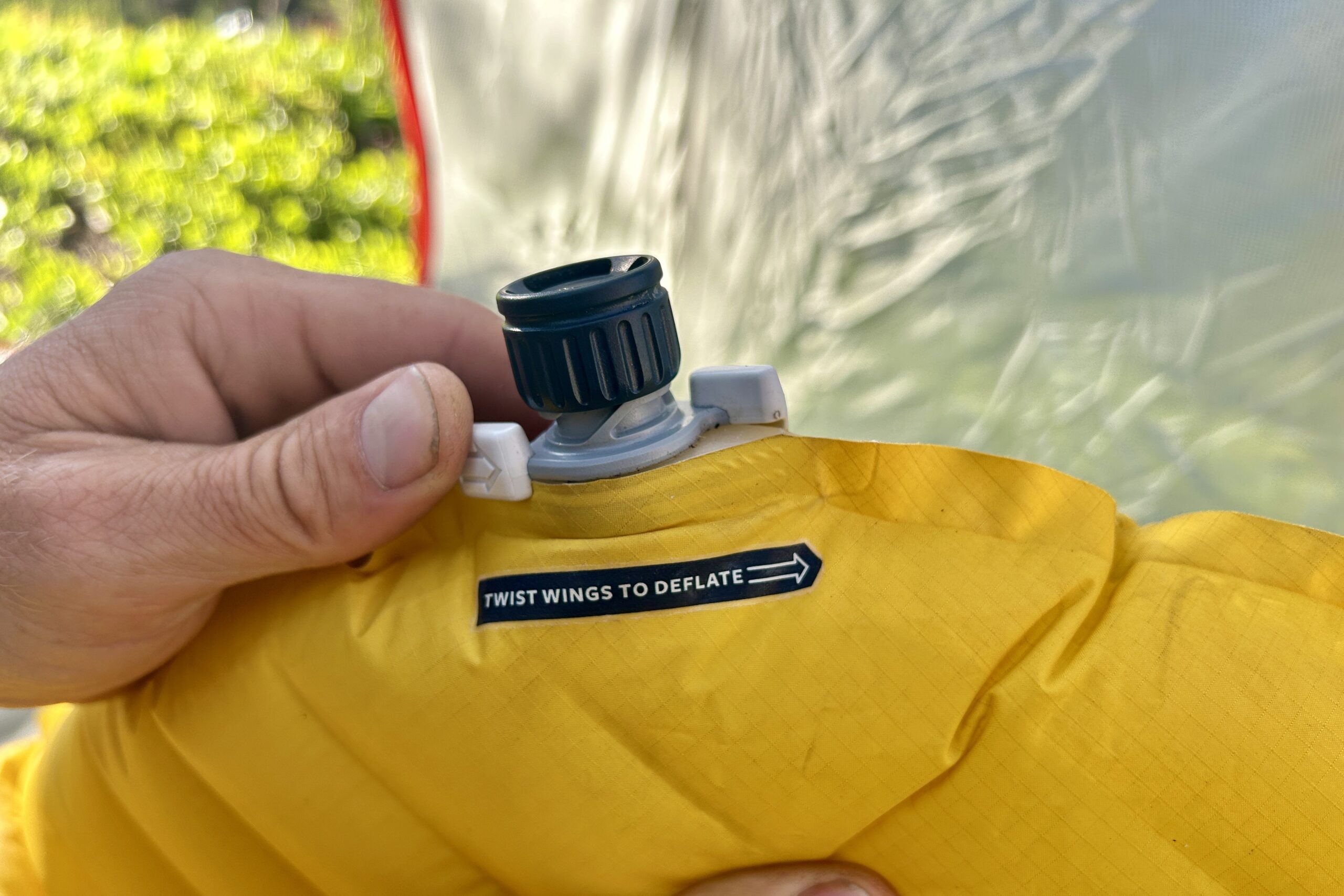 A pair of hands opens the valve of a sleeping pad.