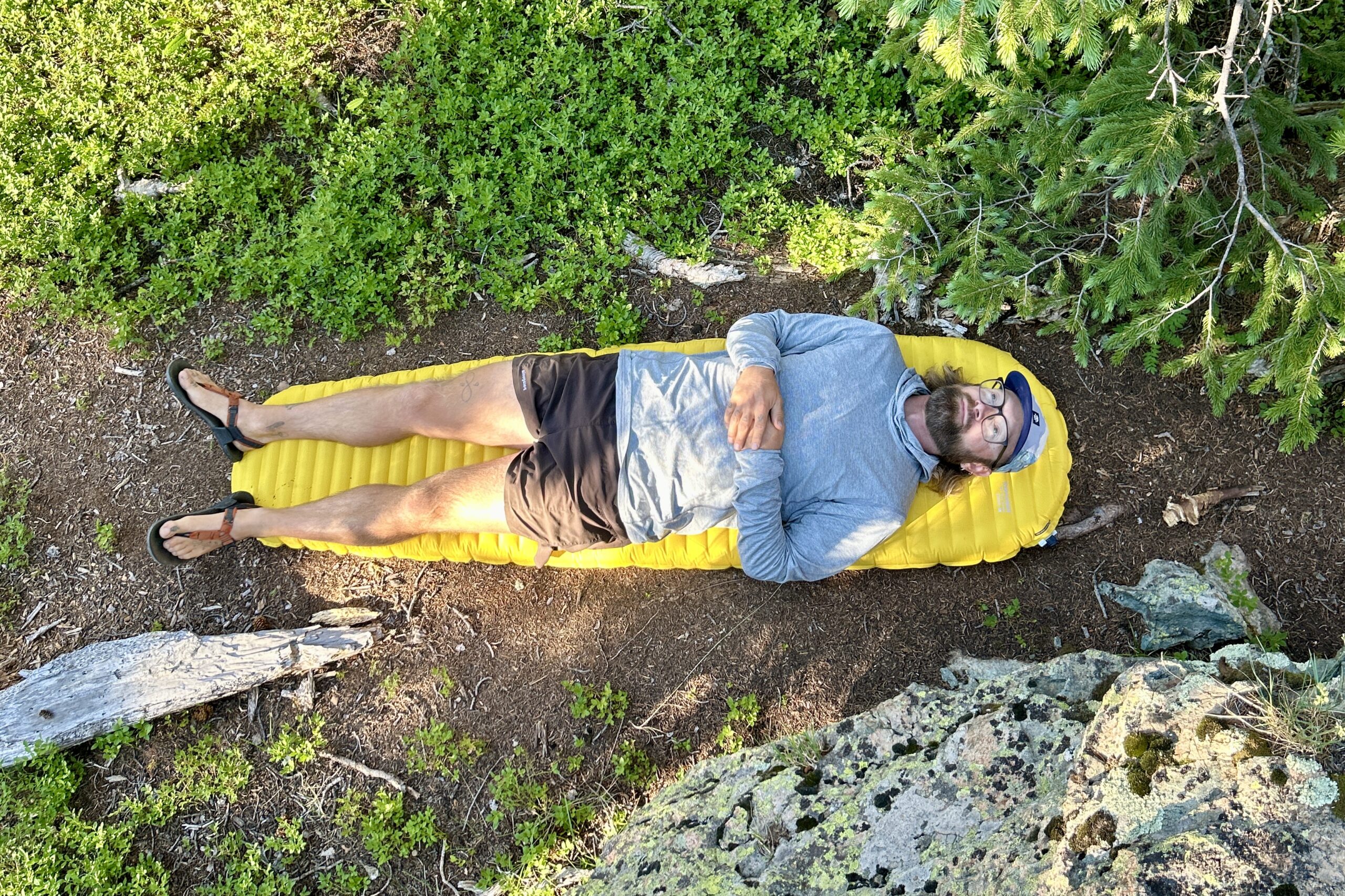 A man is lying on an inflatable mattress on the dirt on a sunny day.