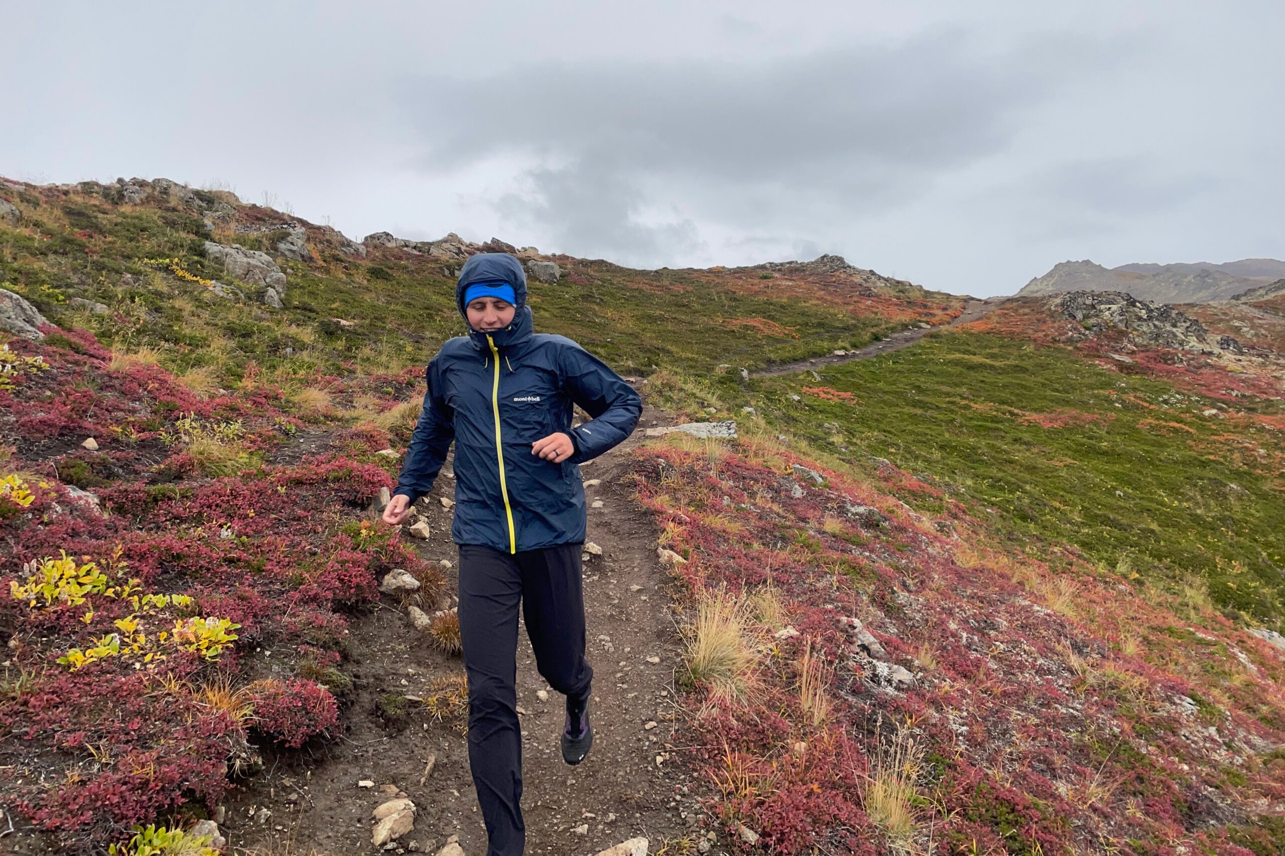 A man runs down a trail wearing a hooded jacket.