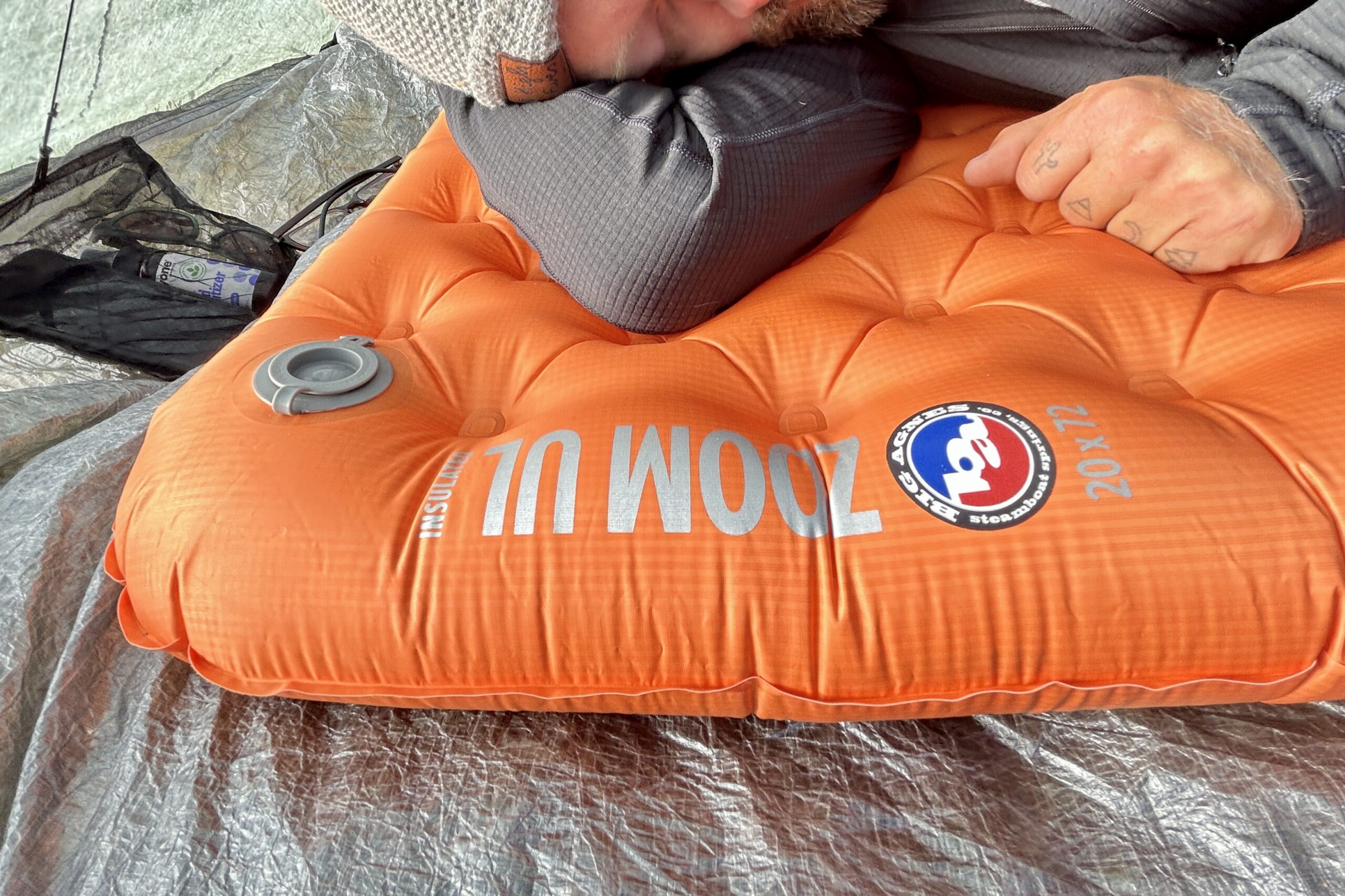 Close up of a man relaxing on an orange sleeping pad in a tent