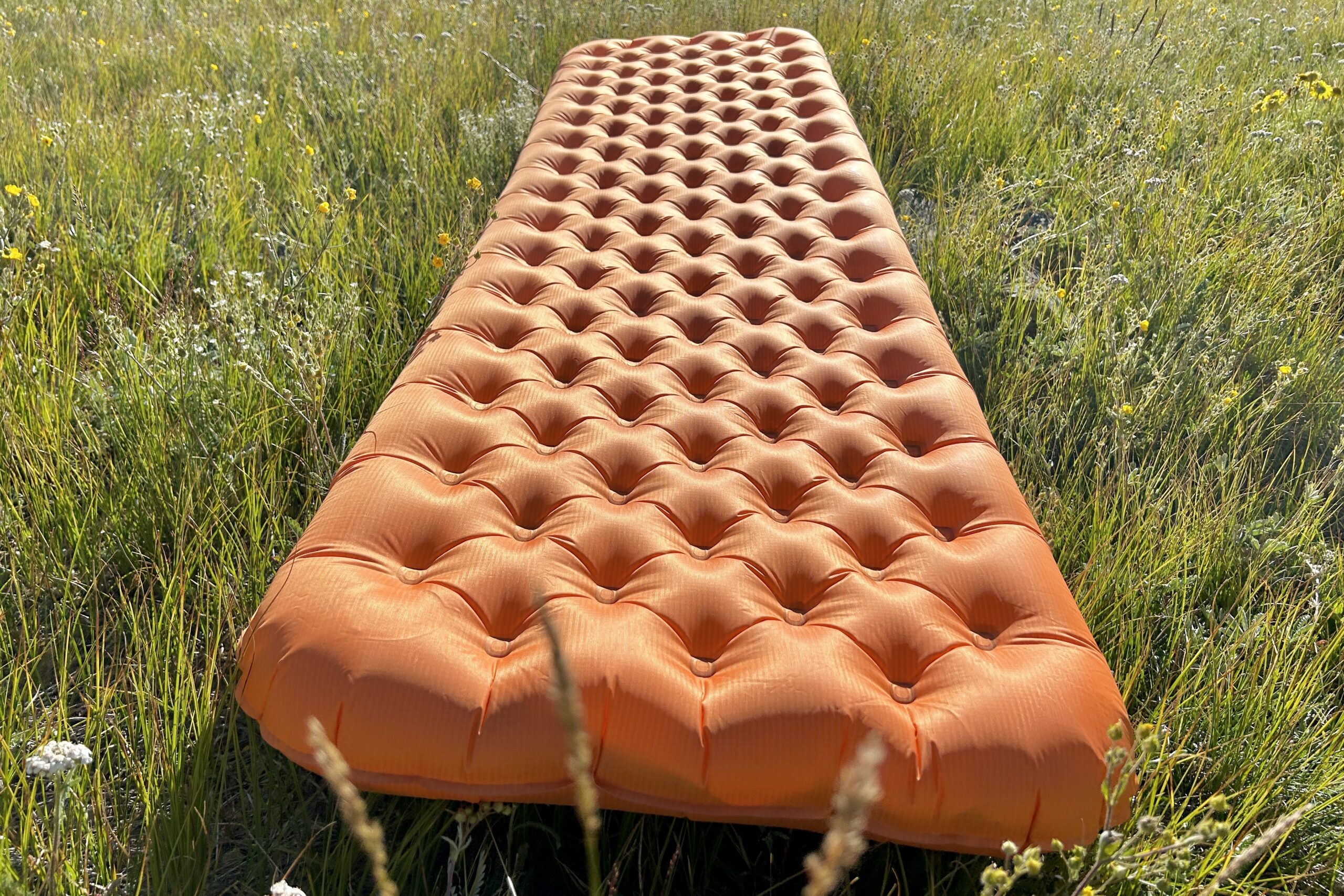 A large orange inflatable mattress laying in a green field