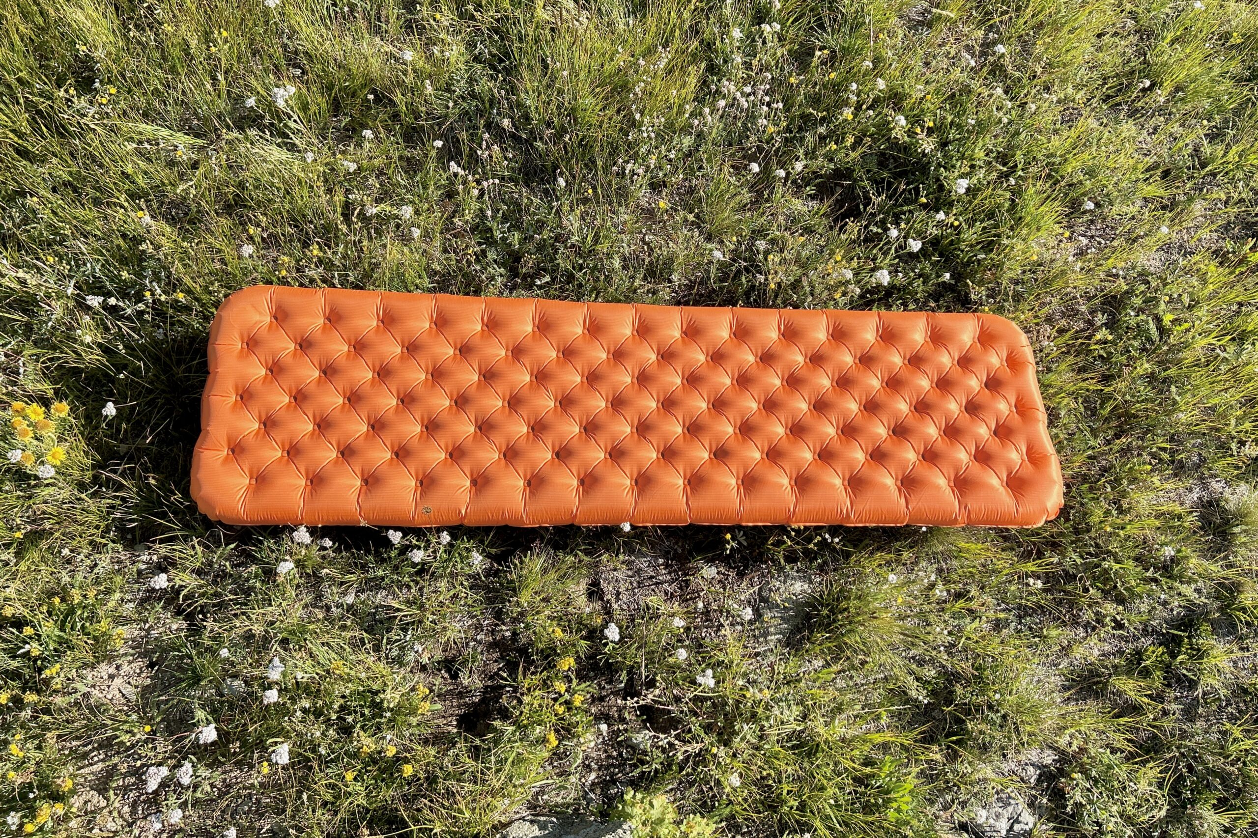 A large orange inflatable mattress laying in a green field