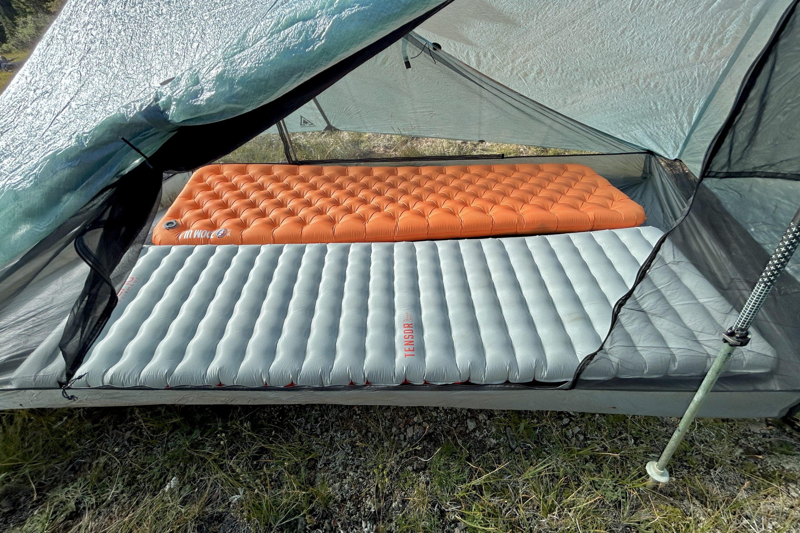 A large orange mattress and large grey inflatable mattresses are setup inside a tent.