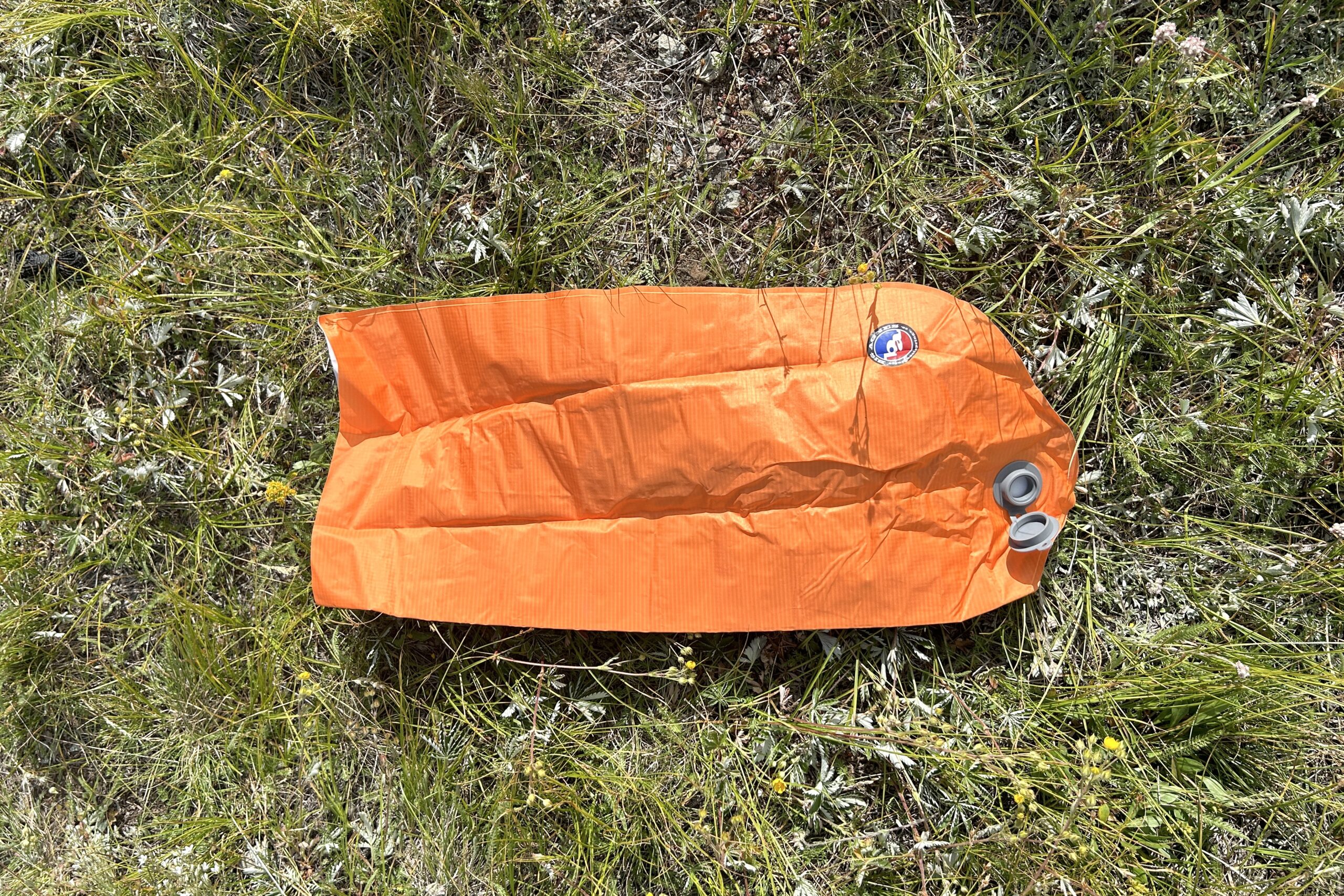 A deflated orange pump sack lies on grass.