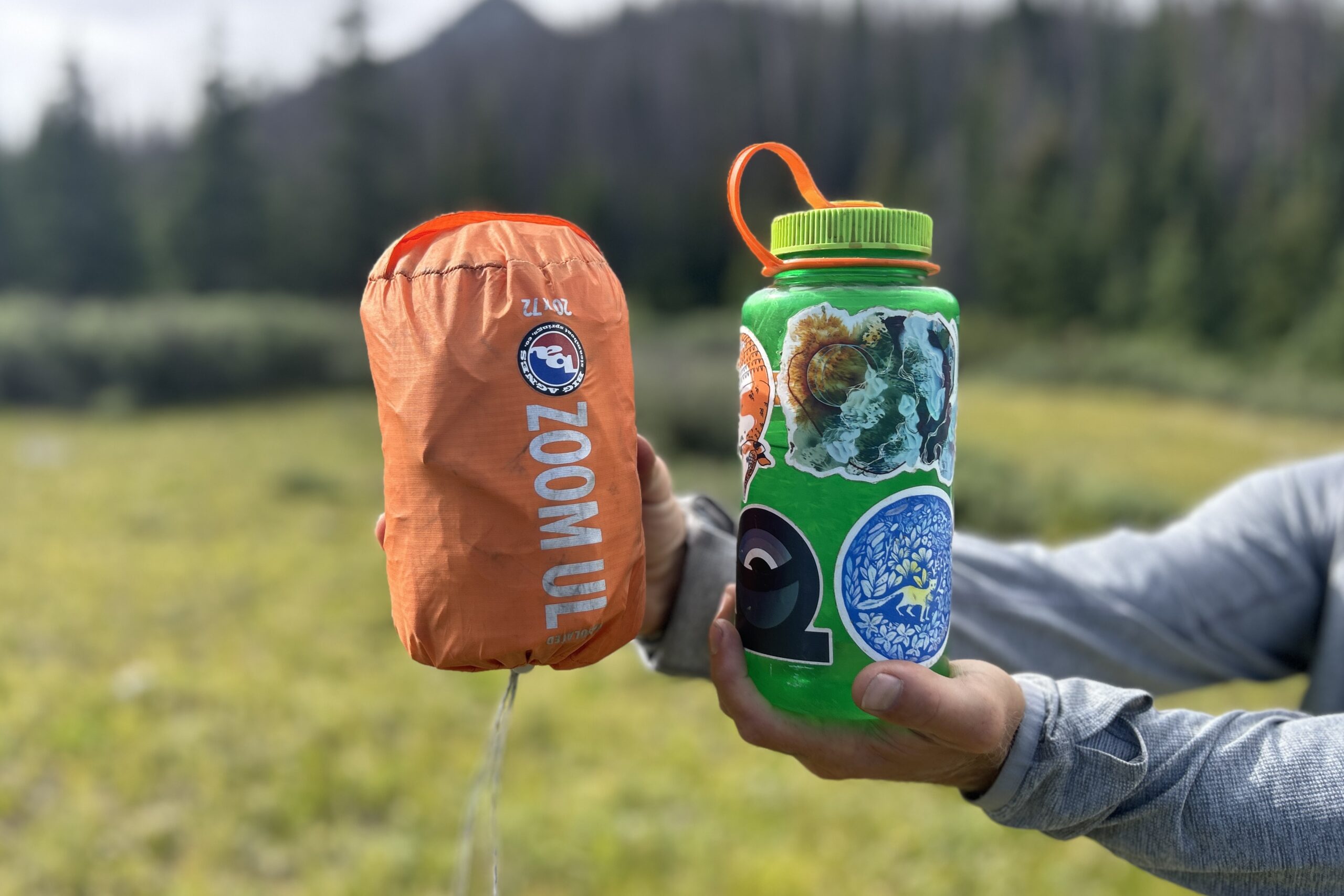 A person holds up an orange sleeping pad in it's compression sack next to a water bottle for a size comparison.