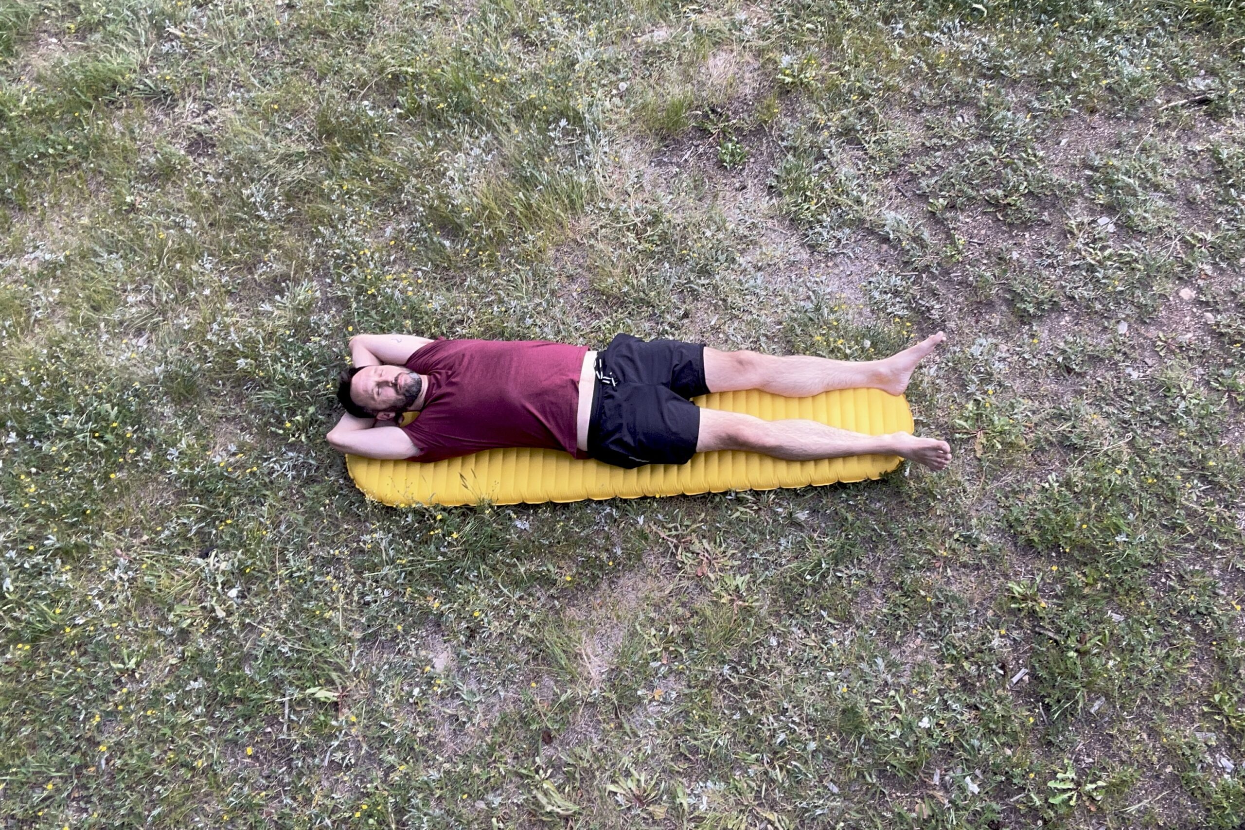 A man is lying on an inflatable mattress on the dirt on a sunny day.