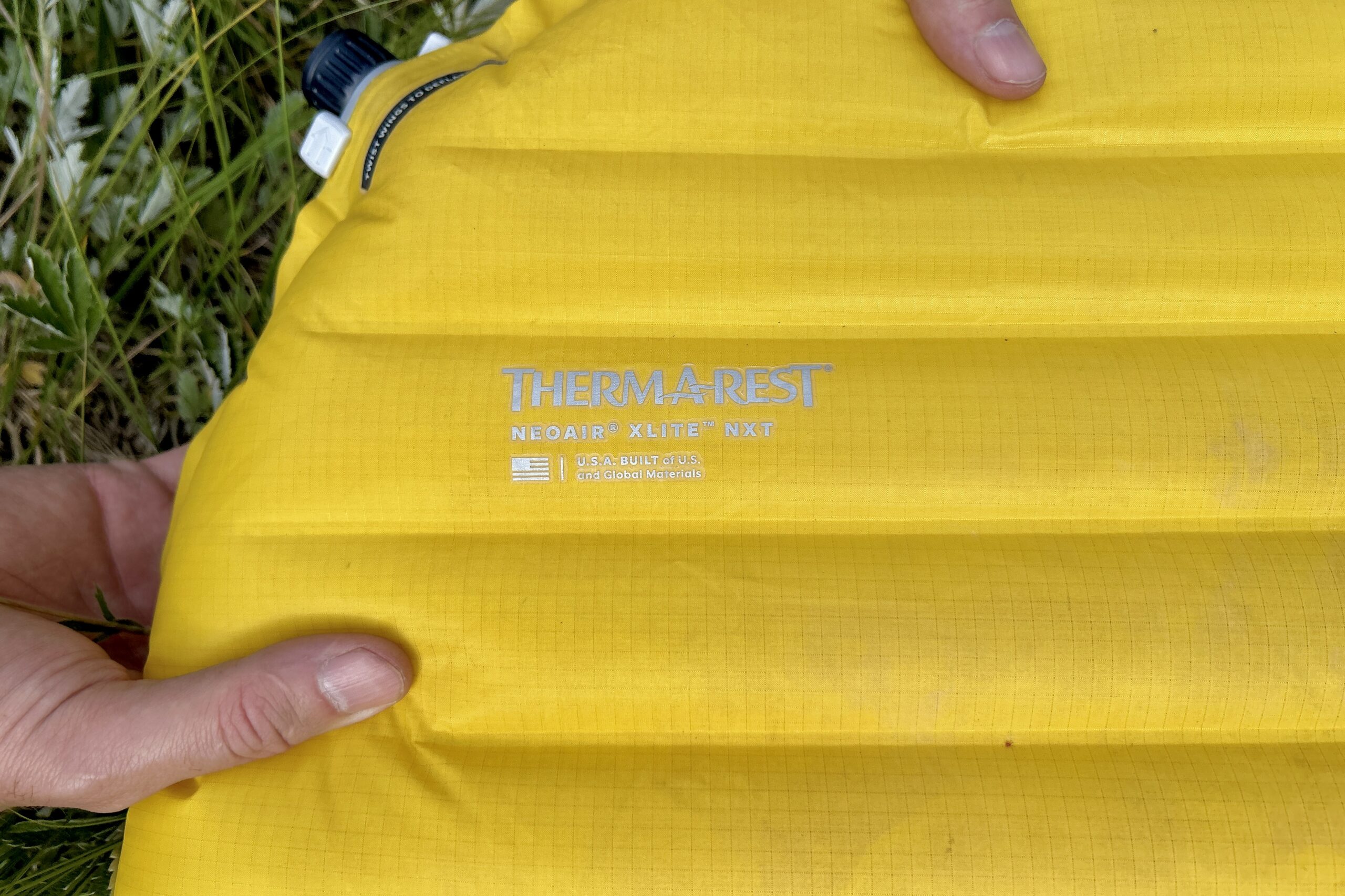 Close up image of two hands holding the top corner of a sleeping pad.