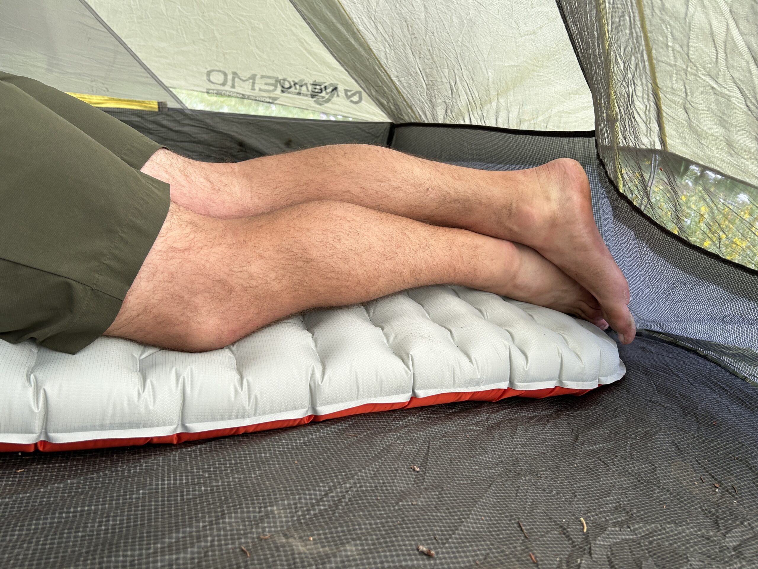 A man's legs from the waist down on an inflatable sleeping pad in a tent.