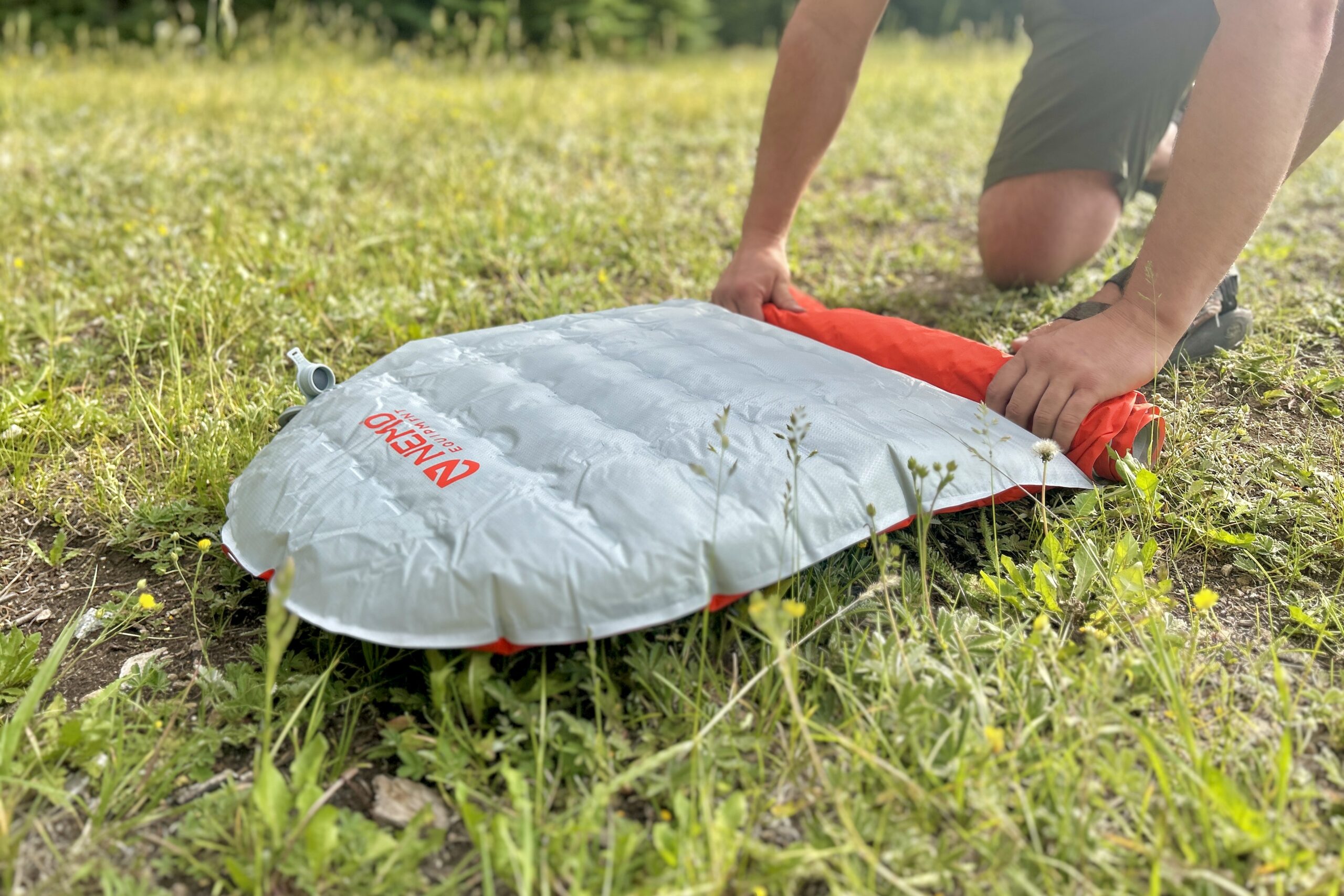 A man rolls up an inflatable sleeping pad on the ground.