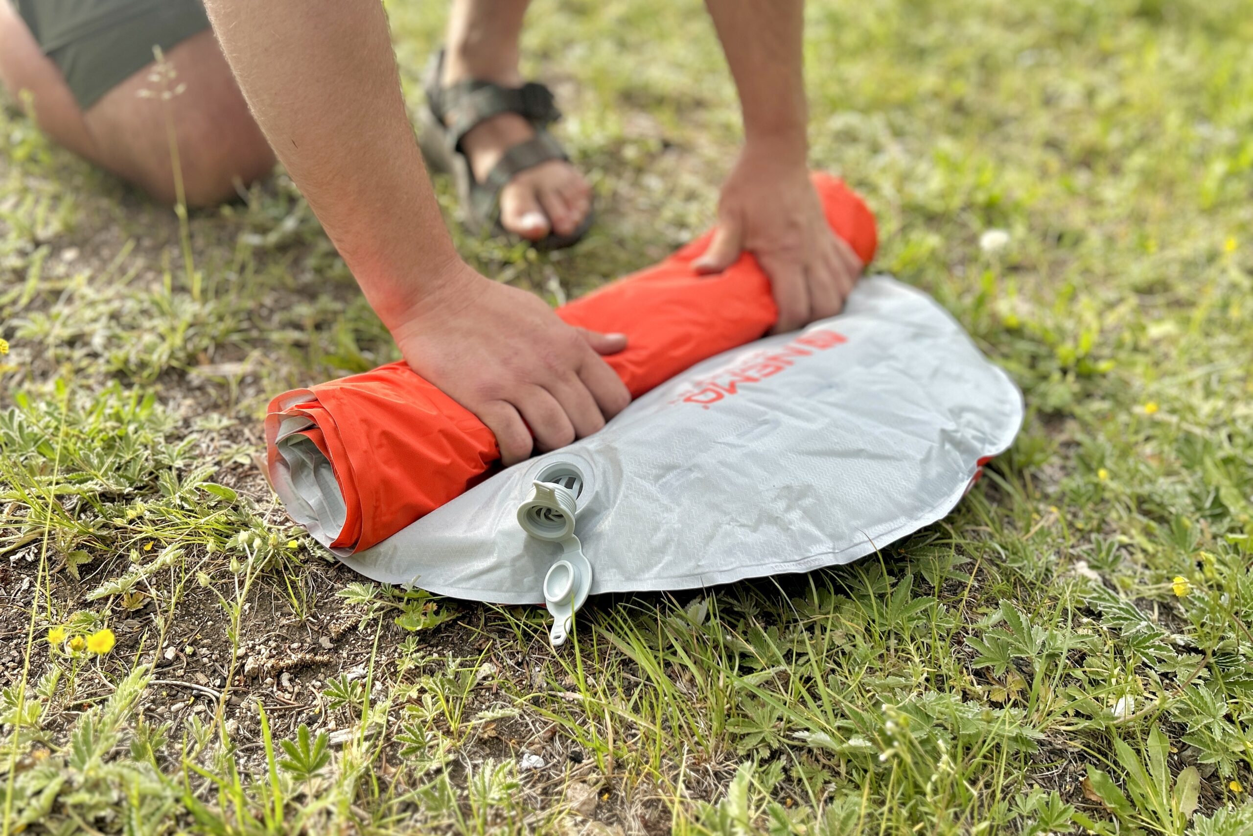 A man rolls up an inflatable sleeping pad on the ground.