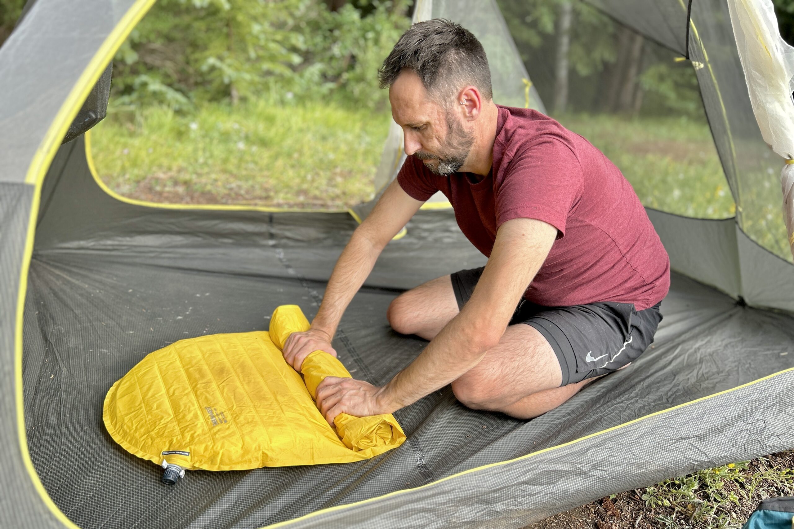 A man rolls up an inflatable sleeping pad in a tent.