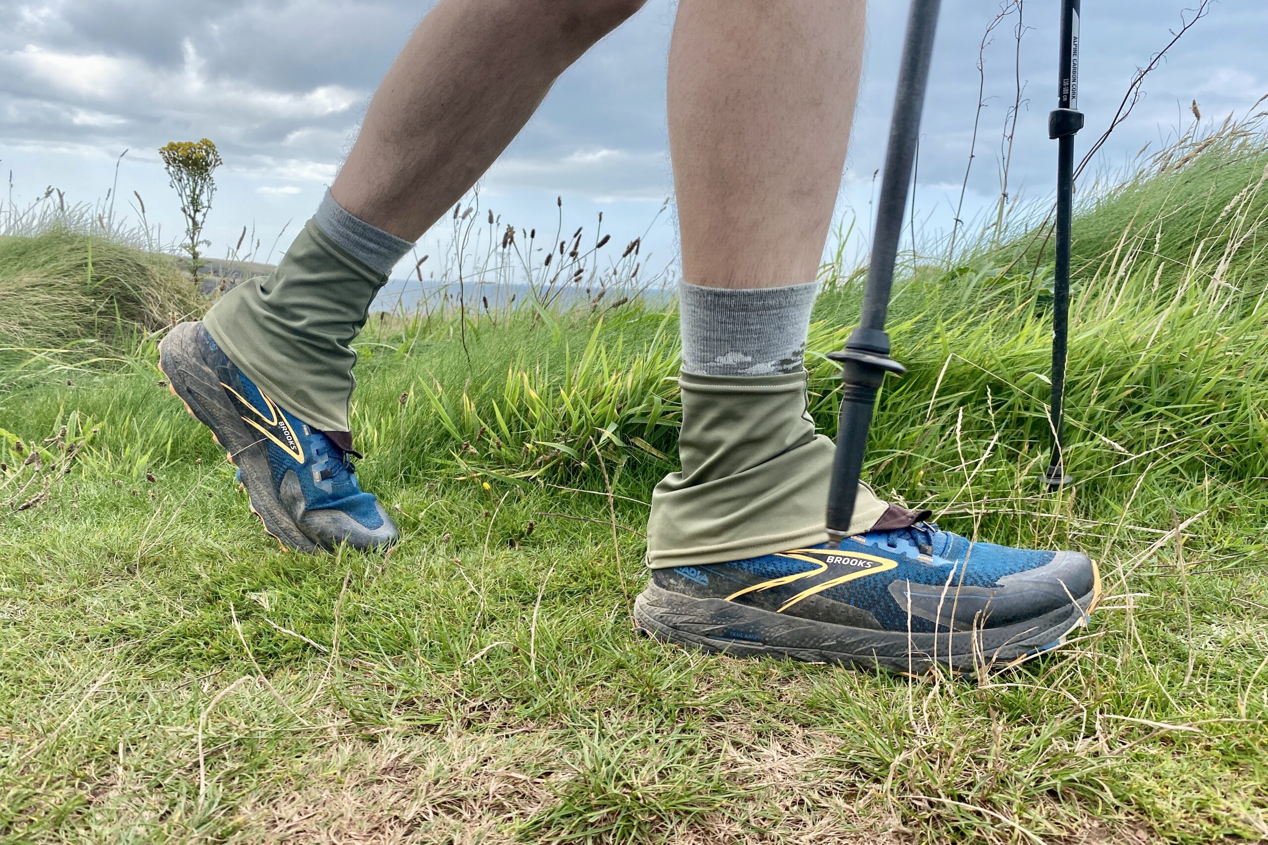 A man takes a step while wearing a pair of trail running shoes with a pair of low gaiters.