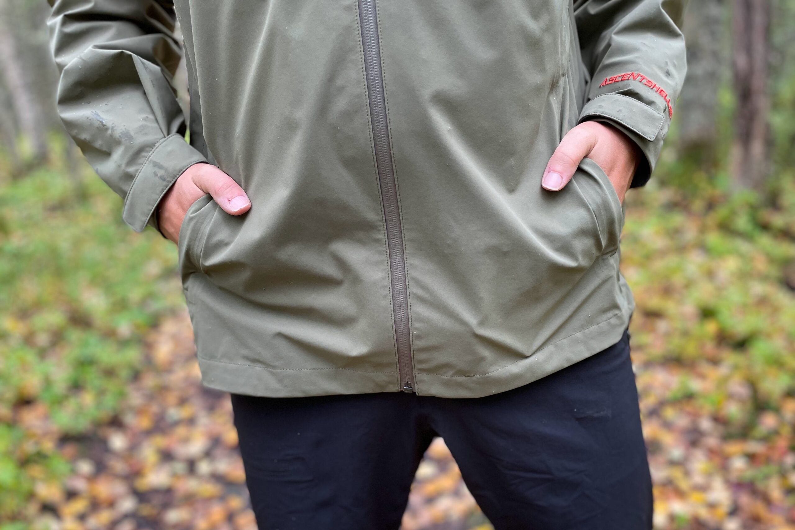 Um close de um homem parado com as mãos nos bolsos de uma capa de chuva.