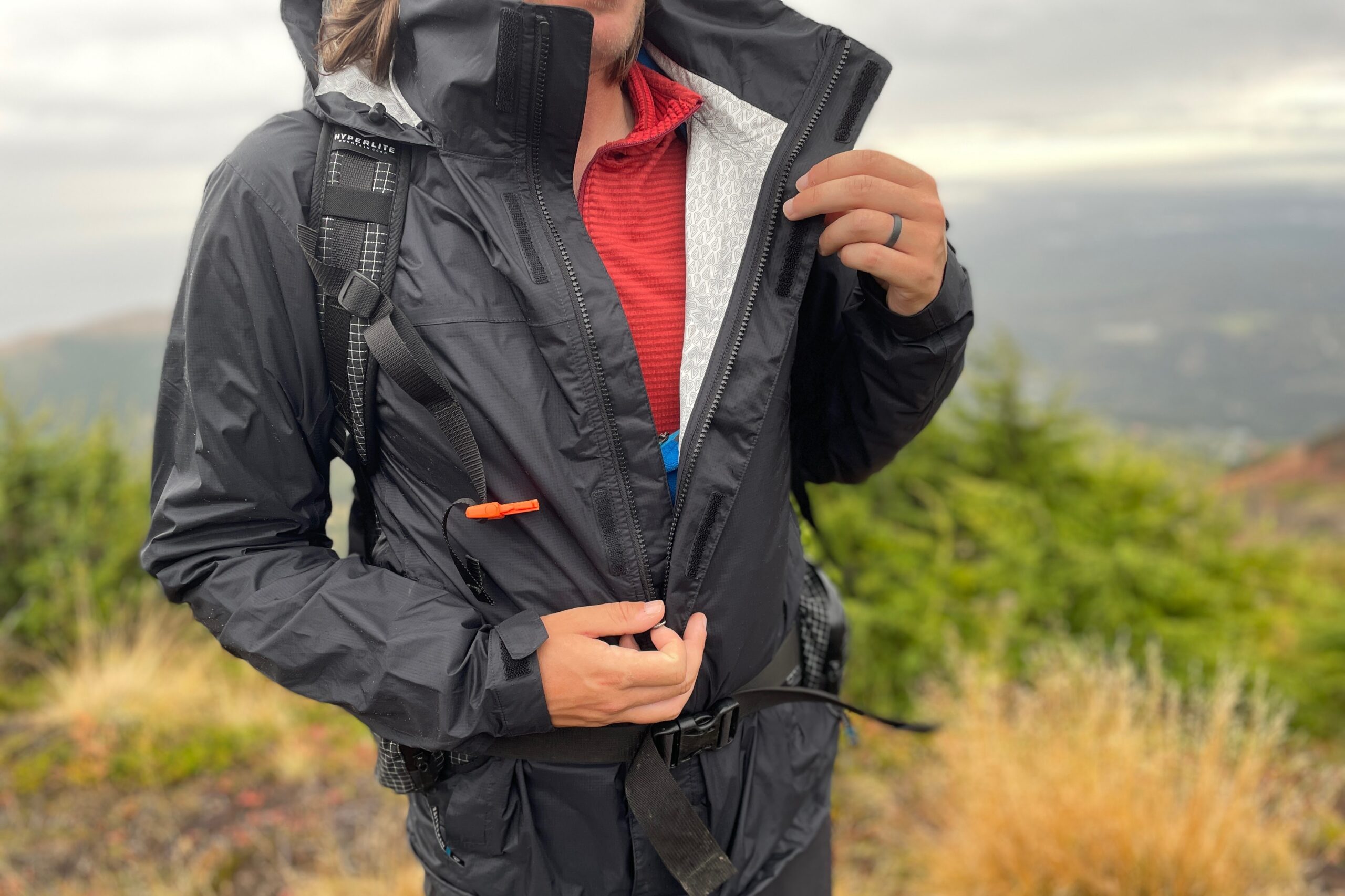 A closeup of a man unzipping his rain jacket.