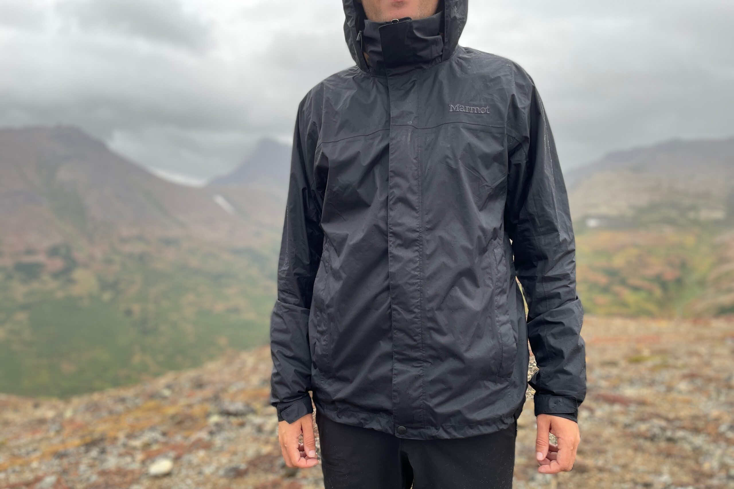 A man faces the camera on a rainy day in the mountains above treeline.