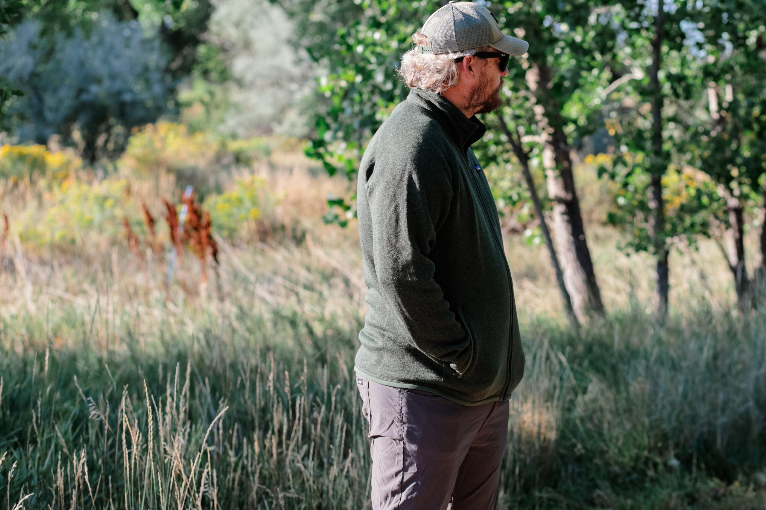 A man wearing a hat stares into the distance with his hands in his pockets.