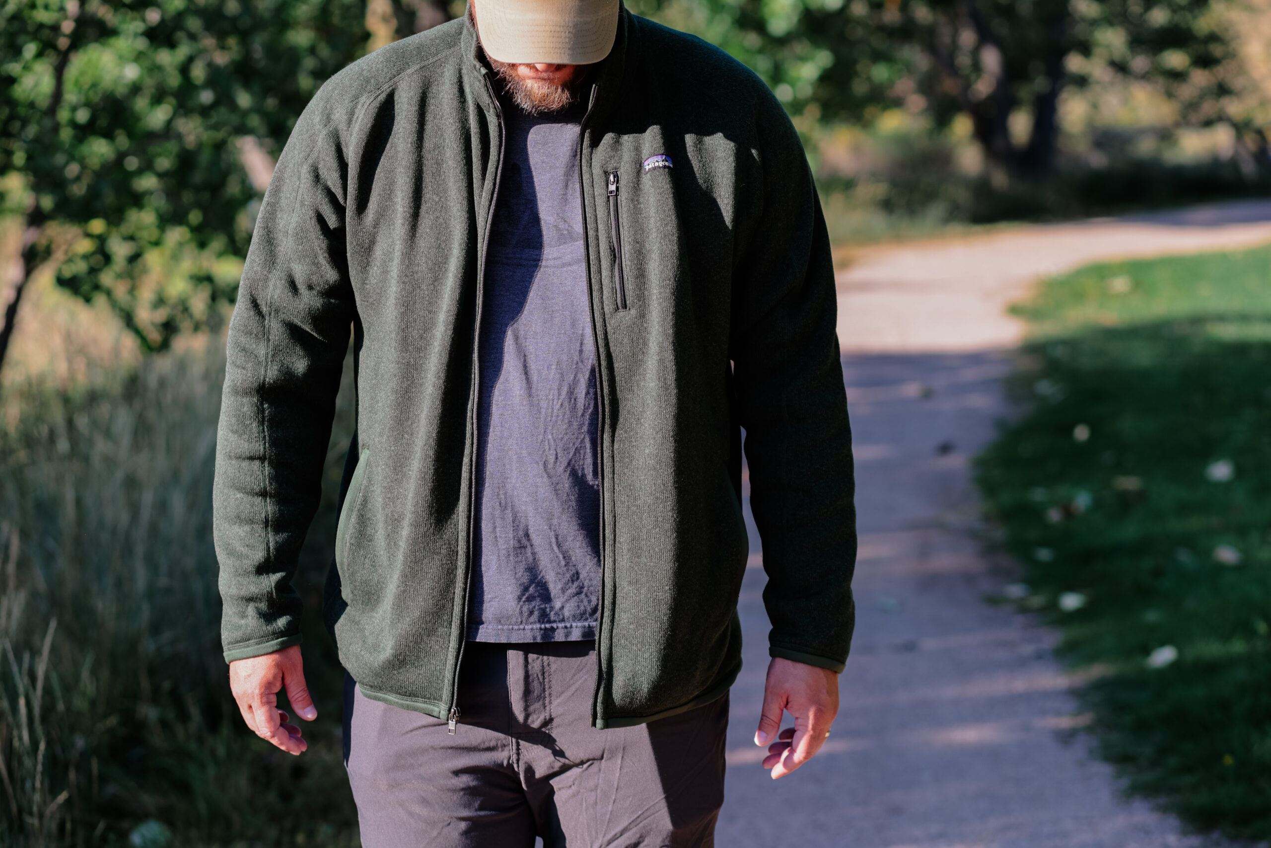 Man walks down a path looking down with an unzipped fleece jacket.