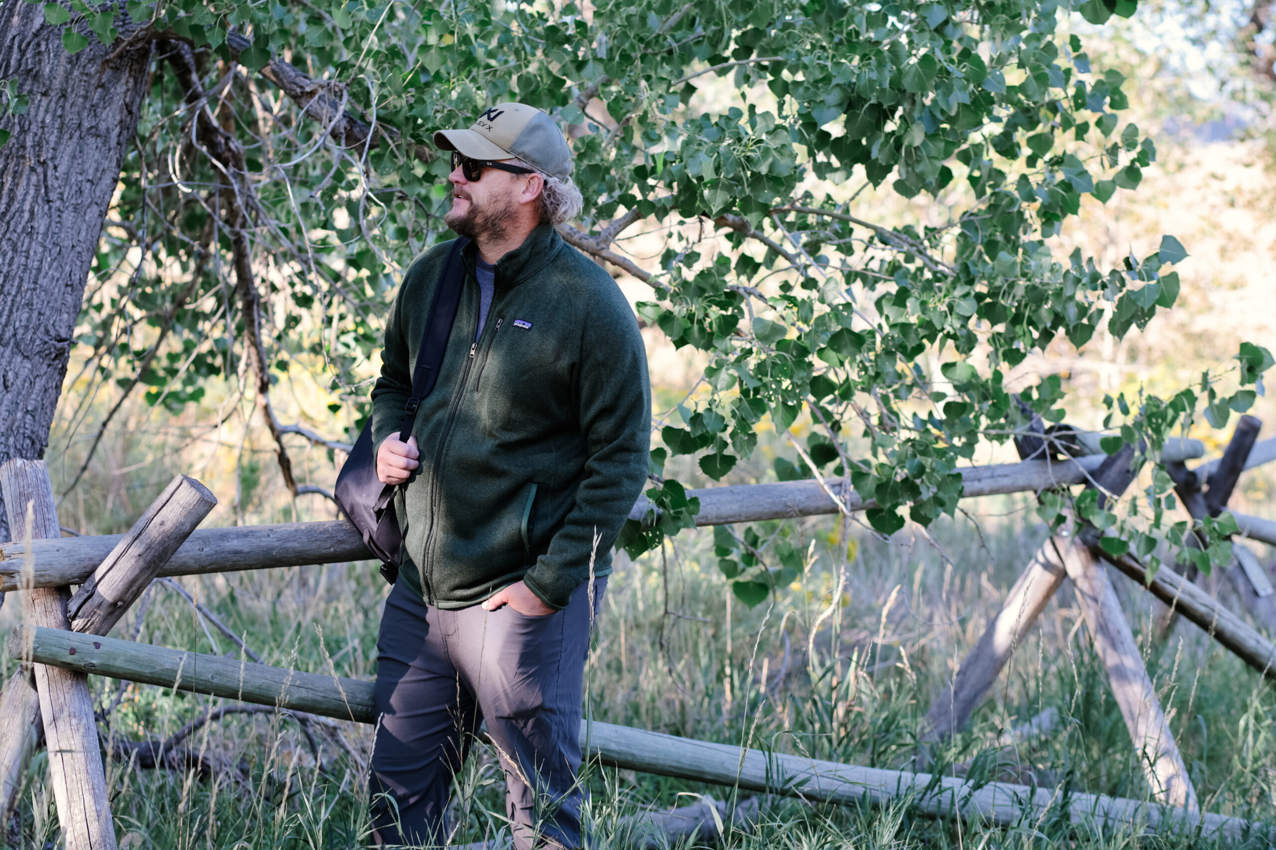 A man carrying a pack stares into the distance while wearing a green hat and fleece jacket.