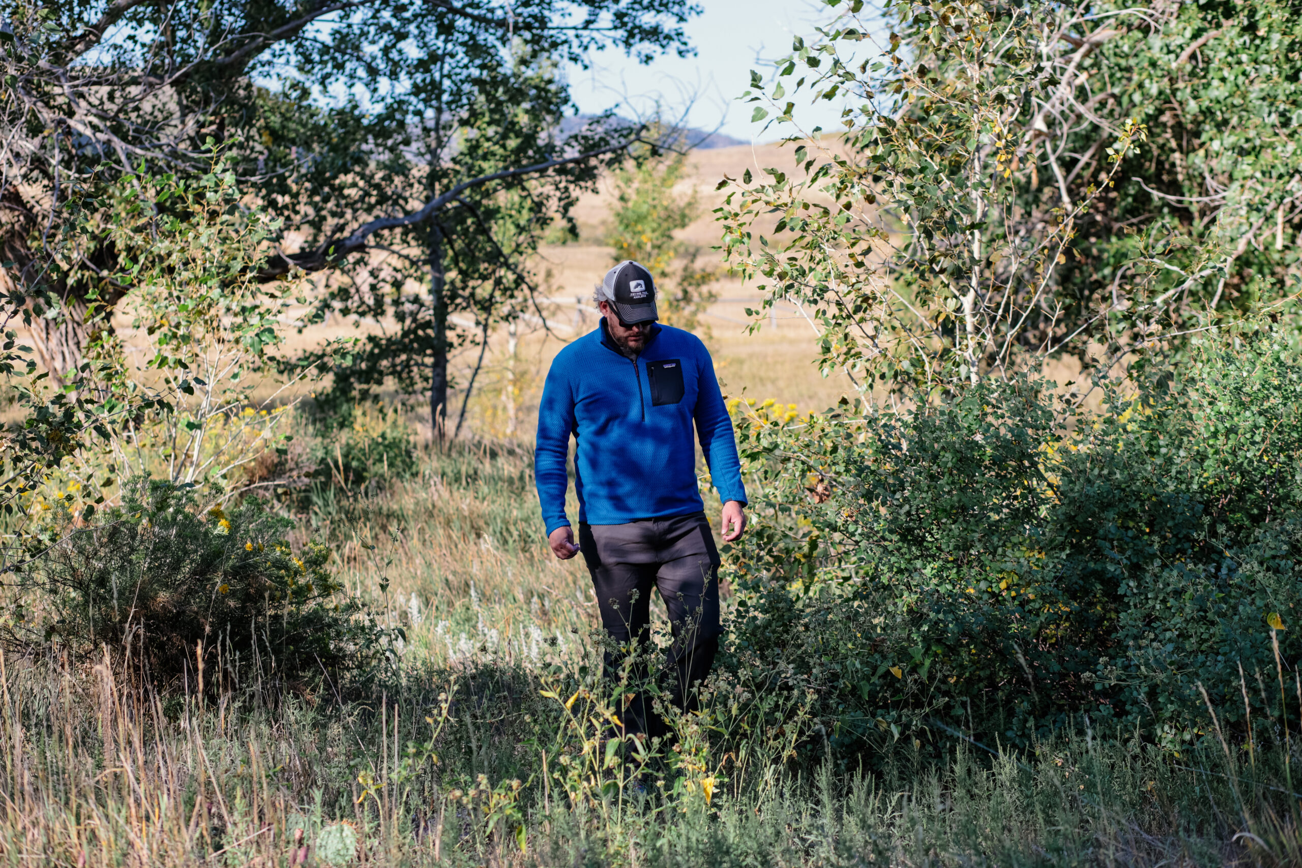 A man walks in the bushes in a blue fleece.