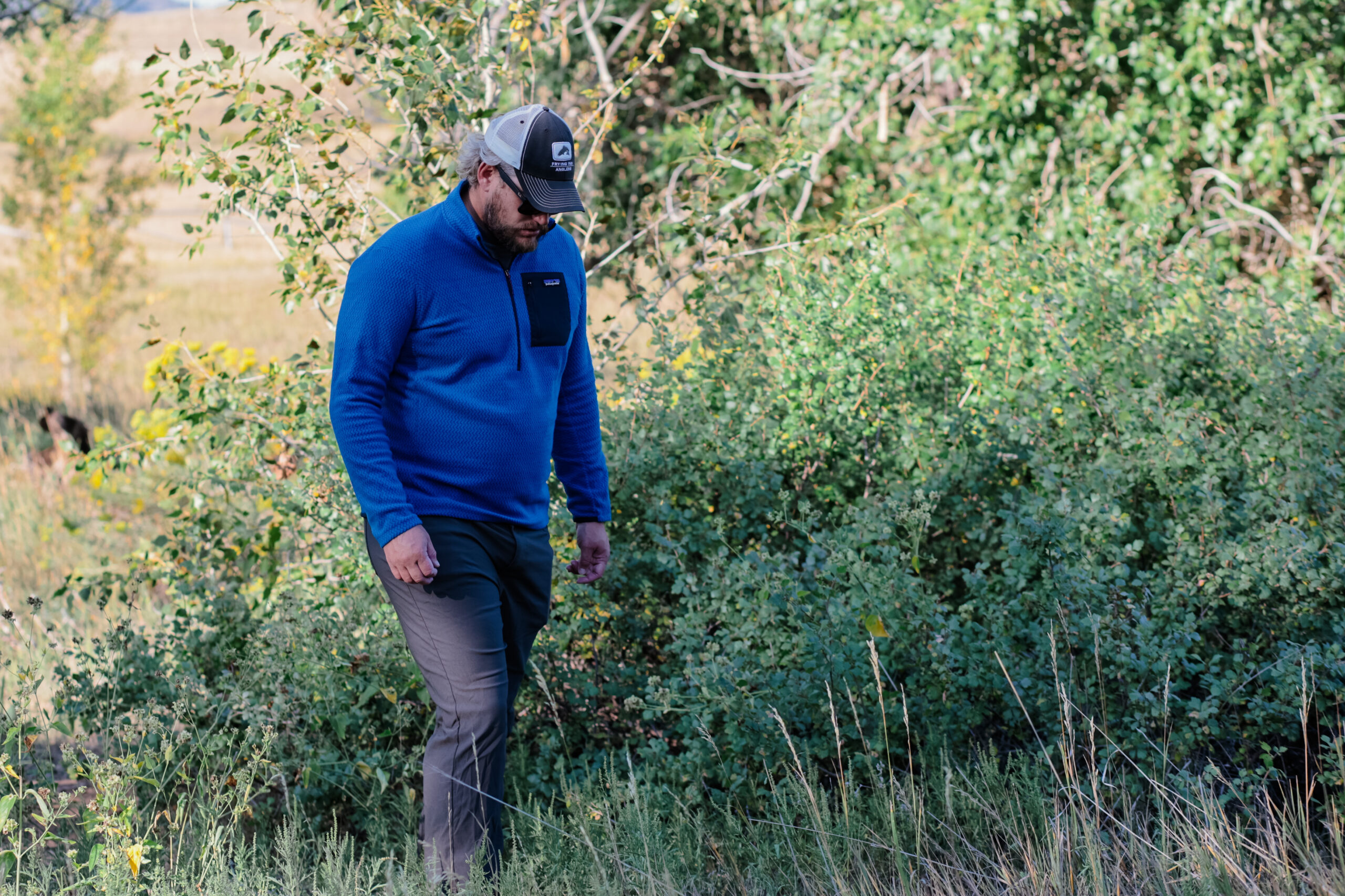 A man hikes through the woods in a hat and blue fleece.