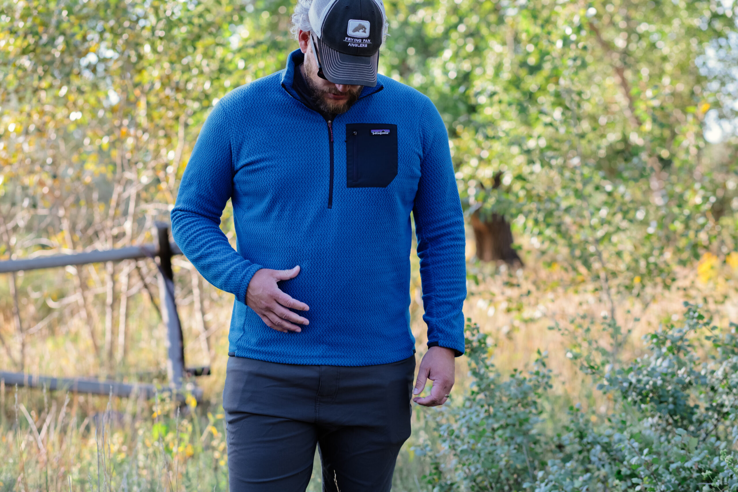 A man walks in the woods wearing a blue fleece.