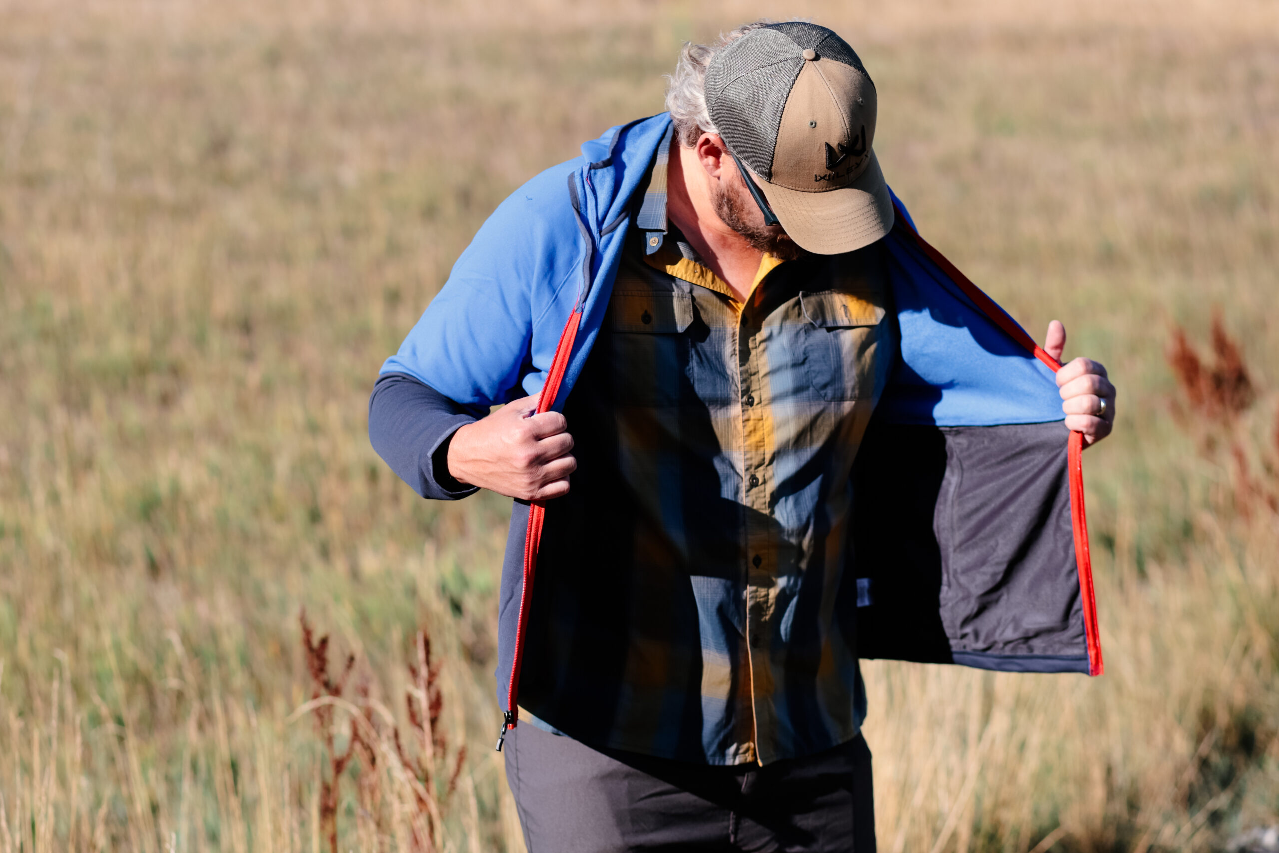 A man opens a jacket in a meadow.