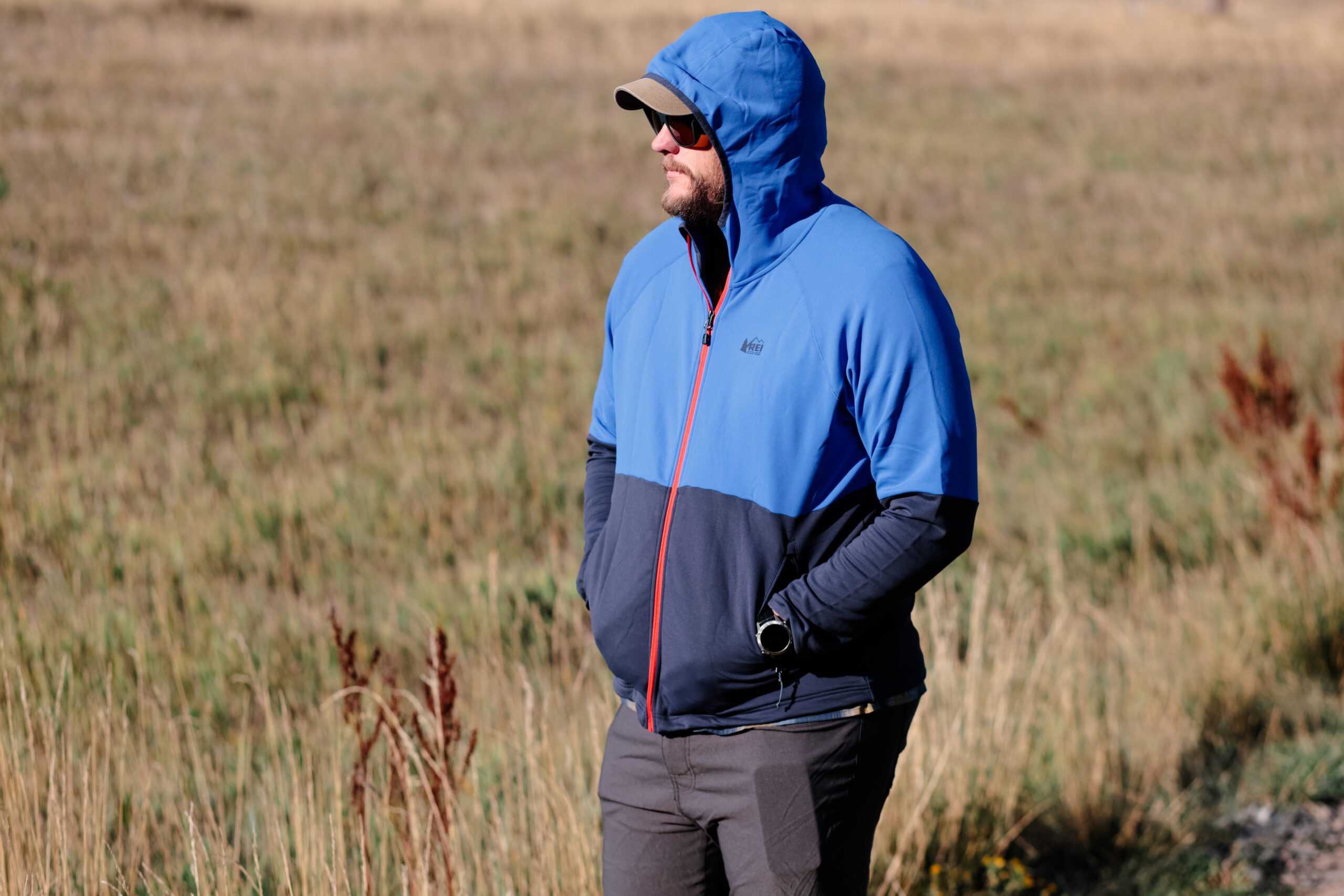 Man with a jacket hood hood up in a sunny alpine meadow.