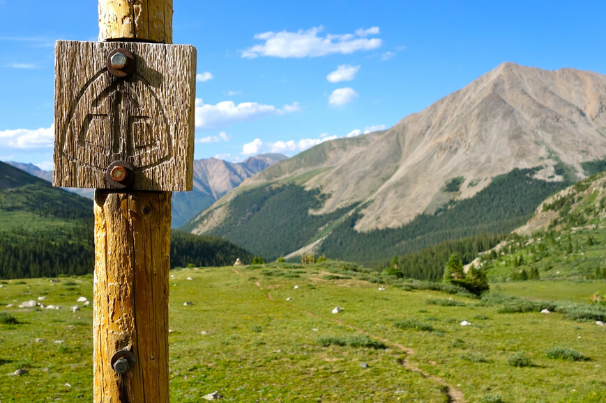 continental divide trail sign post with mountains and meadows behind it